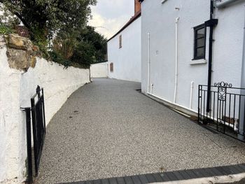 Grey resin driveway with a long white building down the side