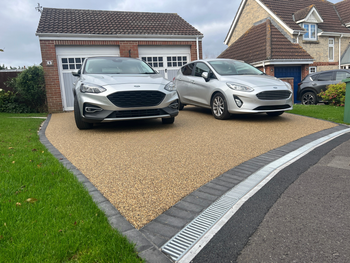 Beige resin drive with grey block paving border, with 2 silver cars parked on top