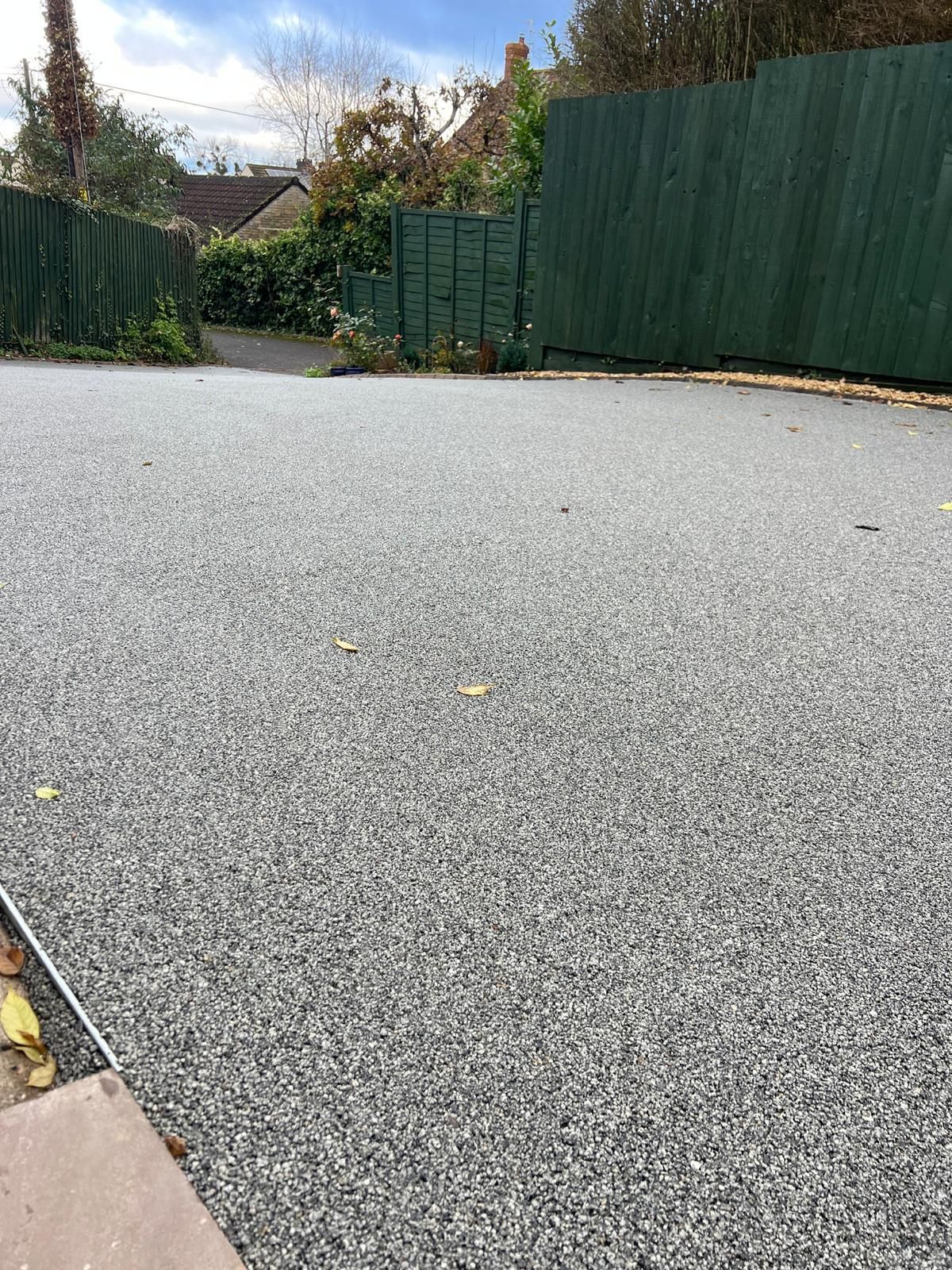 A gray gravel driveway with a green fence in the background.