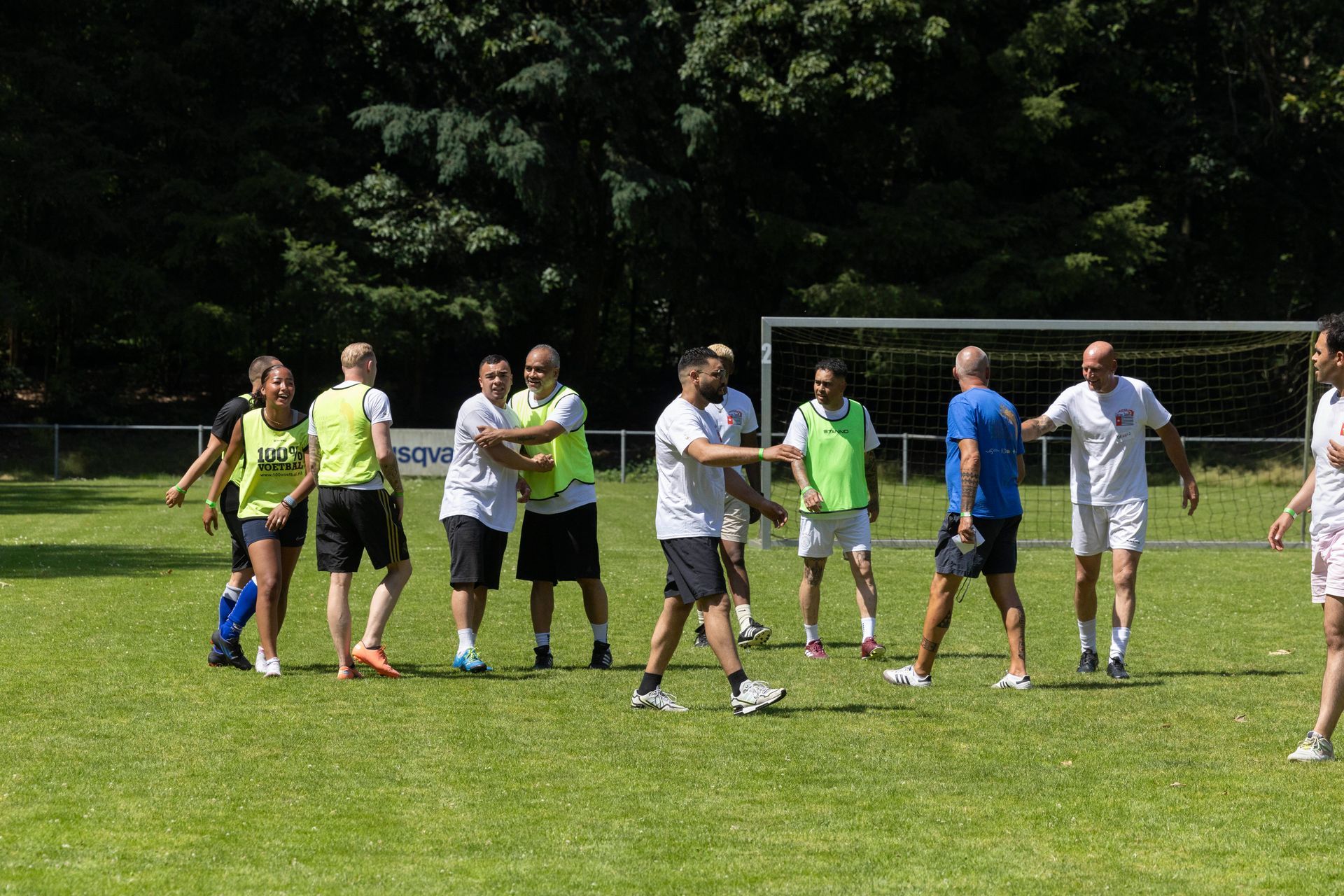 Mensen in sportkleding die met elkaar in gesprek zijn op een grasveld voor een voetbaldoel.