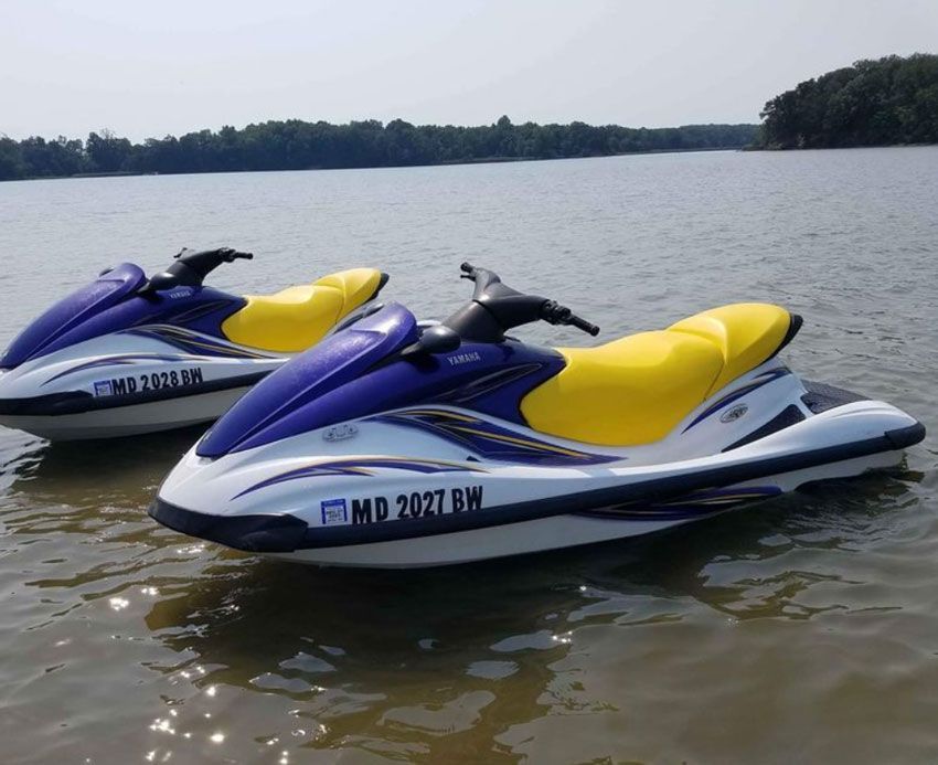 Two blue-and-yellow jet skis floating on a calm lake near a wooded shore
