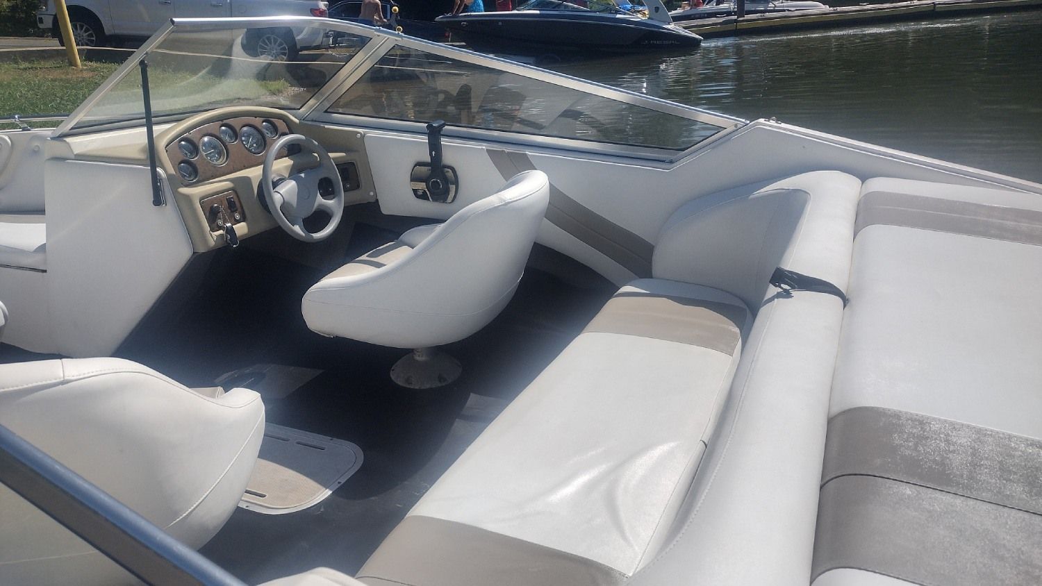 White-and-gray boat interior with steering wheel and cushioned seating on calm water.