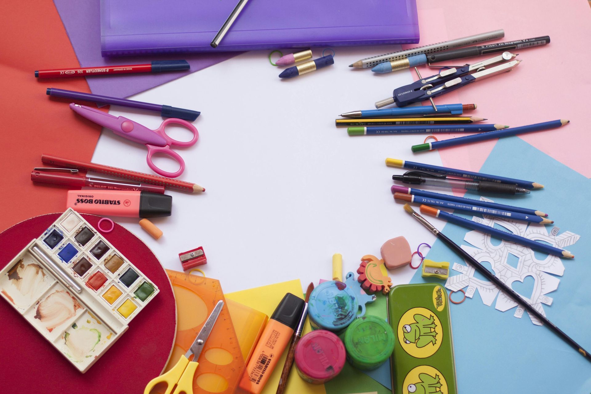 Colorful art supplies arranged on a white background: paints, pencils, pens, scissors, paper.