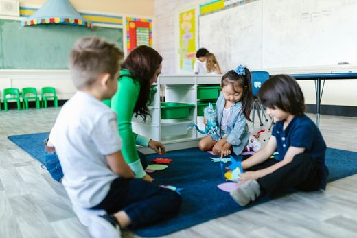 Teacher and children on rug in classroom playing with colorful shapes.