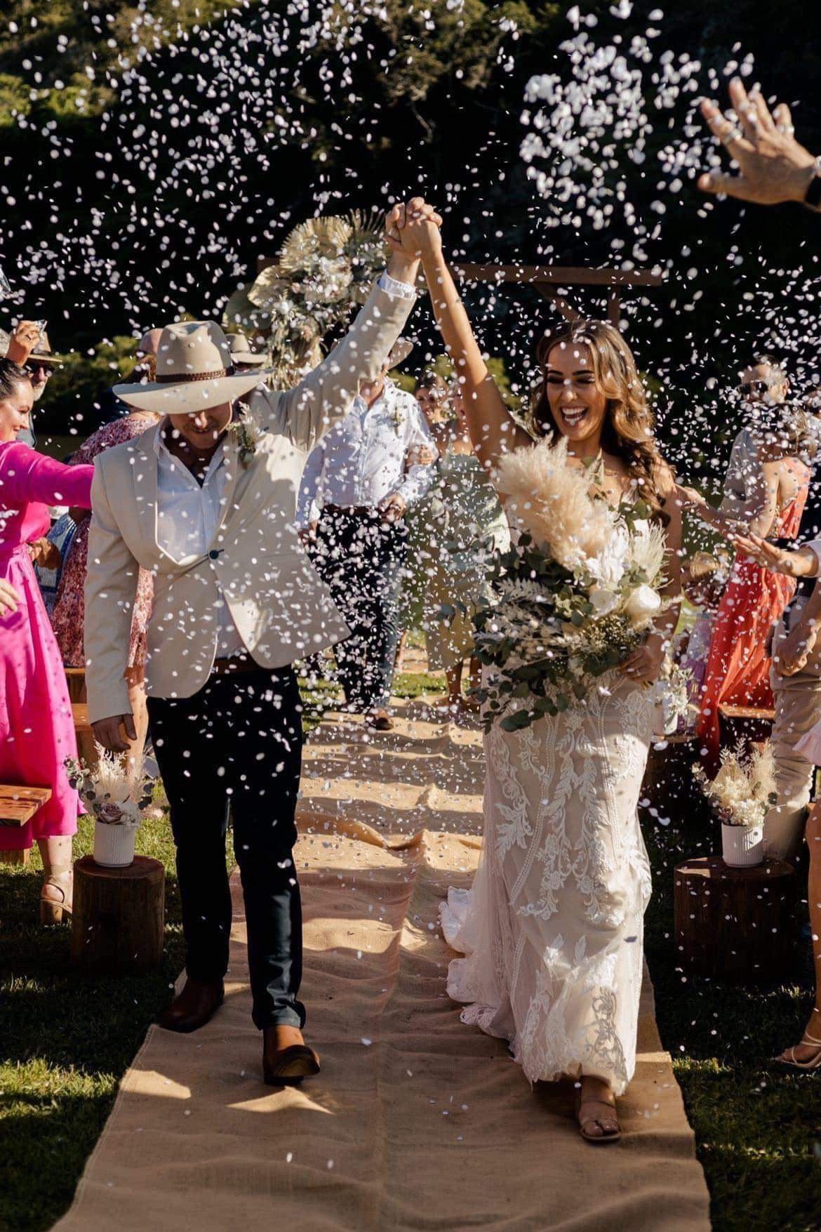 A bride and groom are walking down the aisle surrounded by confetti. — Vanity Skin and Beauty Forster in Forster, NSW