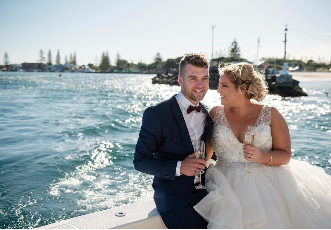 A bride and groom are sitting on a boat holding champagne glasses. — Vanity Skin and Beauty Forster in Forster, NSW