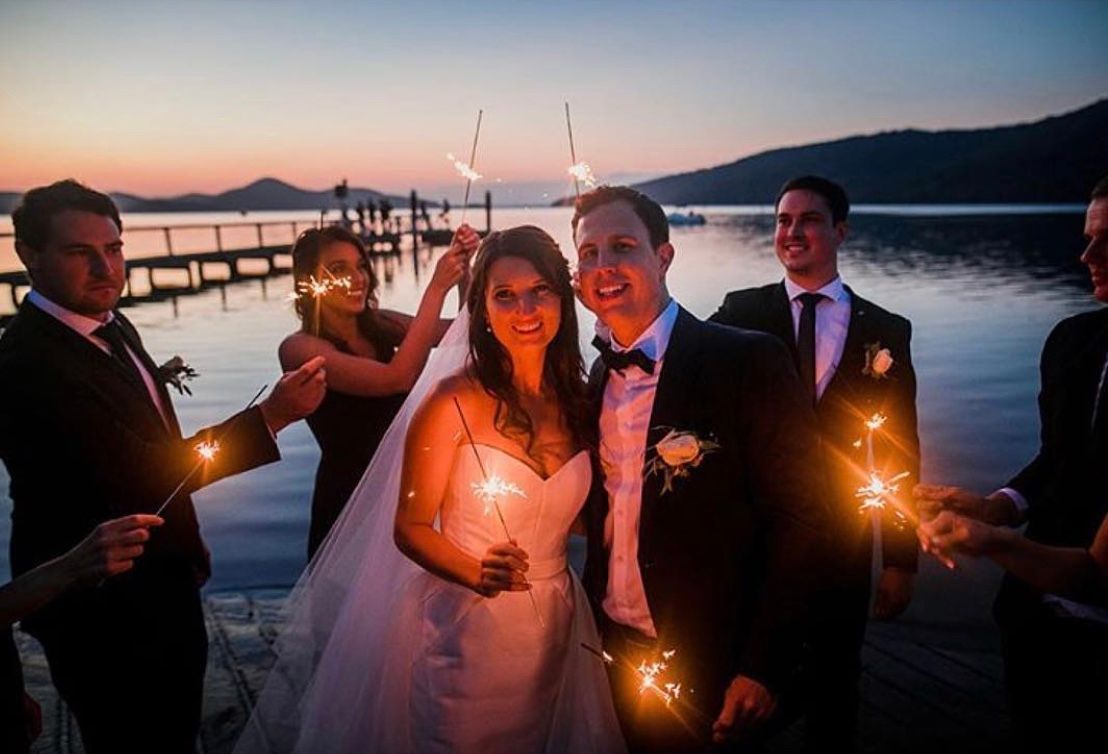 A bride and groom are posing for a picture with their wedding party holding sparklers. — Vanity Skin and Beauty Forster in Forster, NSW