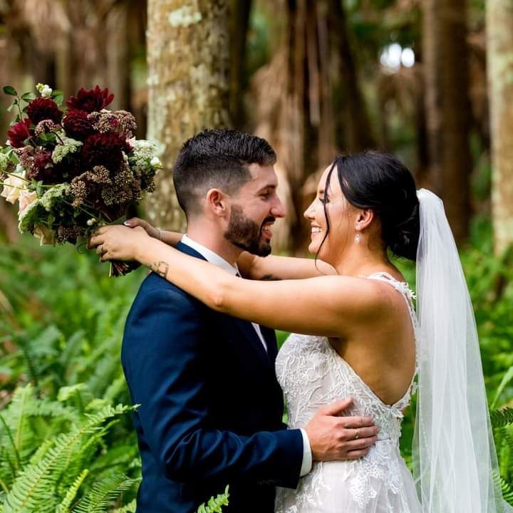 A bride and groom are hugging in the woods and the bride is holding a bouquet of flowers. — Vanity Skin and Beauty Forster in Forster, NSW