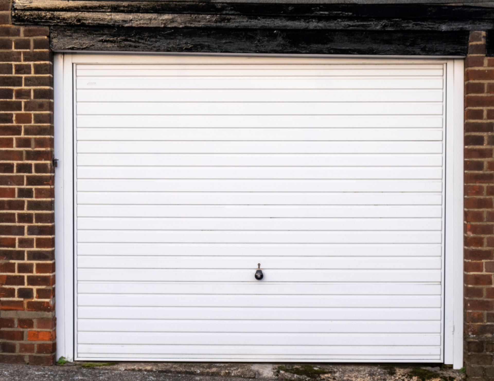 A white garage door is against a brick wall.