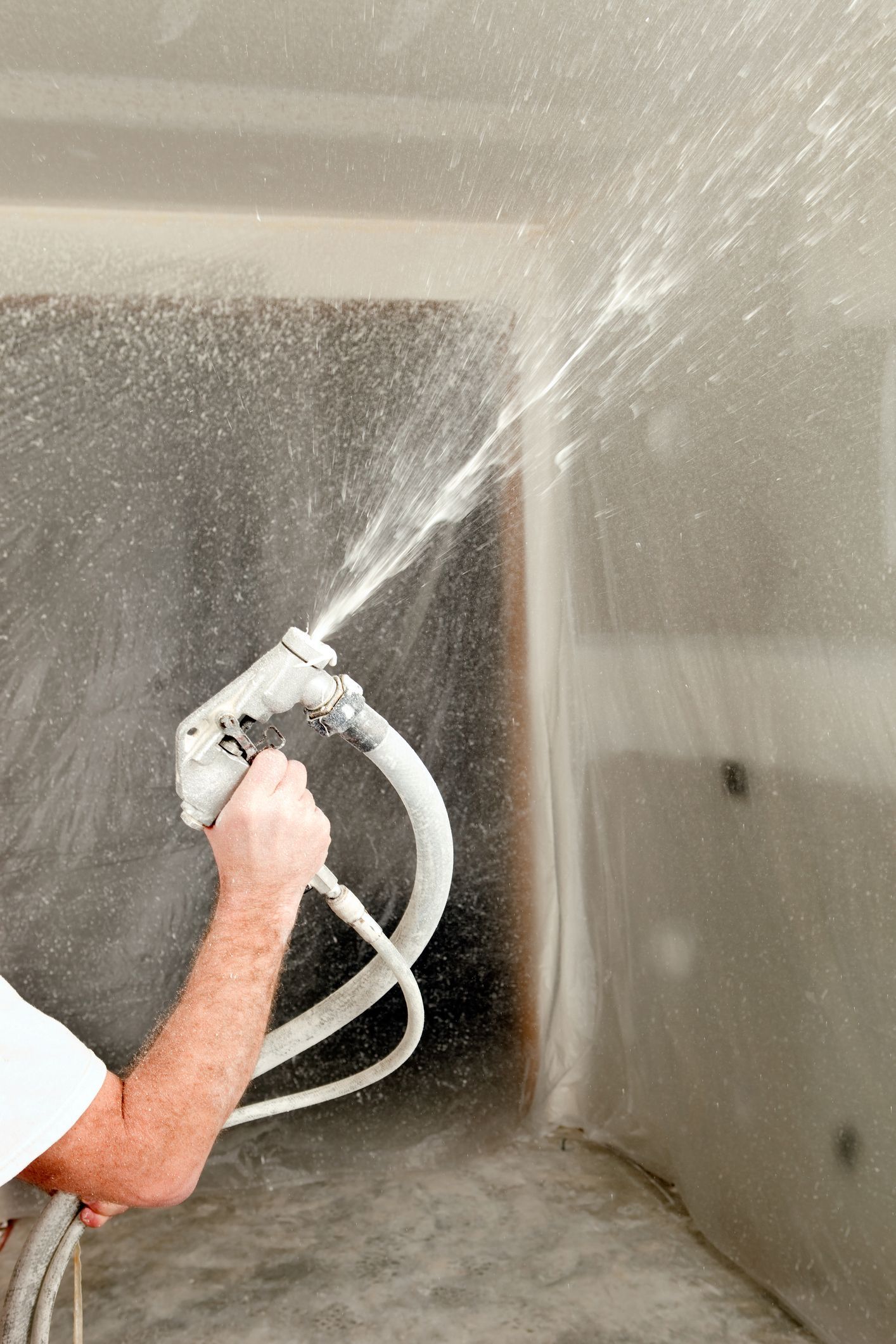 A man is spraying white paint onto a wall in a room.