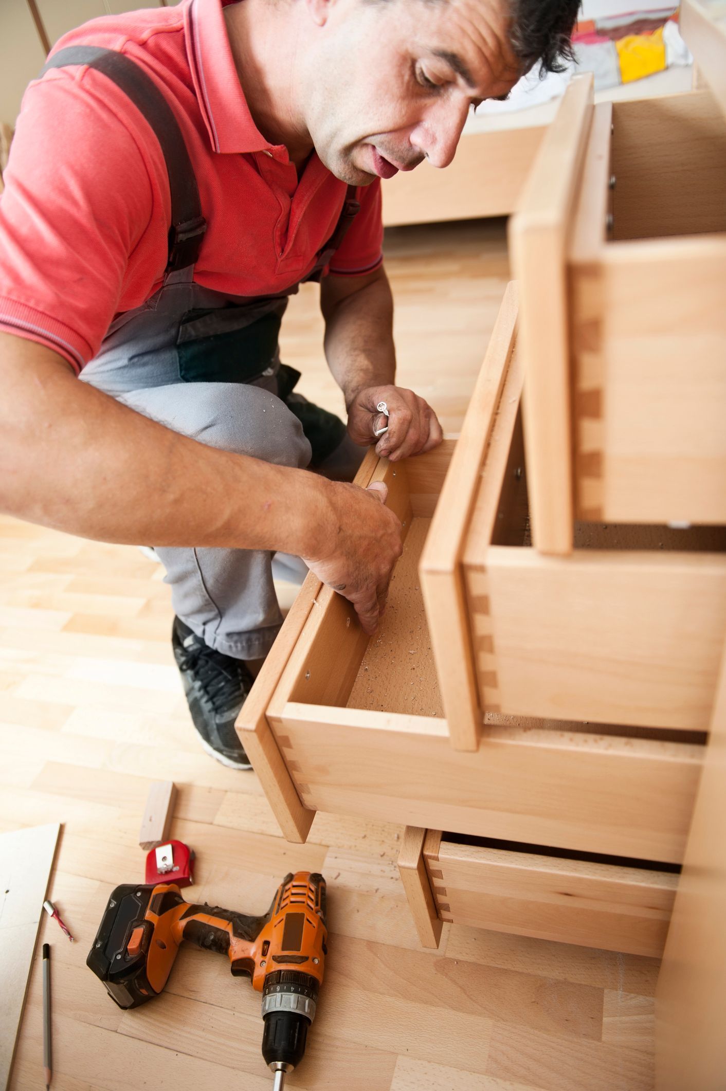 A man is working on a wooden cabinet with a drill.