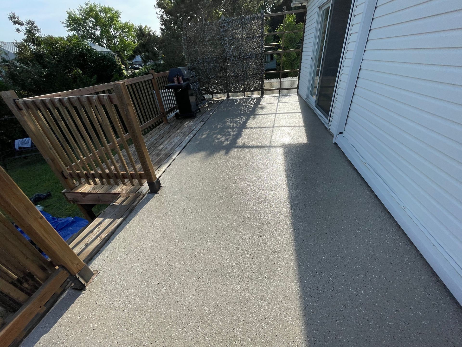 Une terrasse avec une surface lisse et mouchetée à côté d'une maison blanche et d'une balustrade en bois.