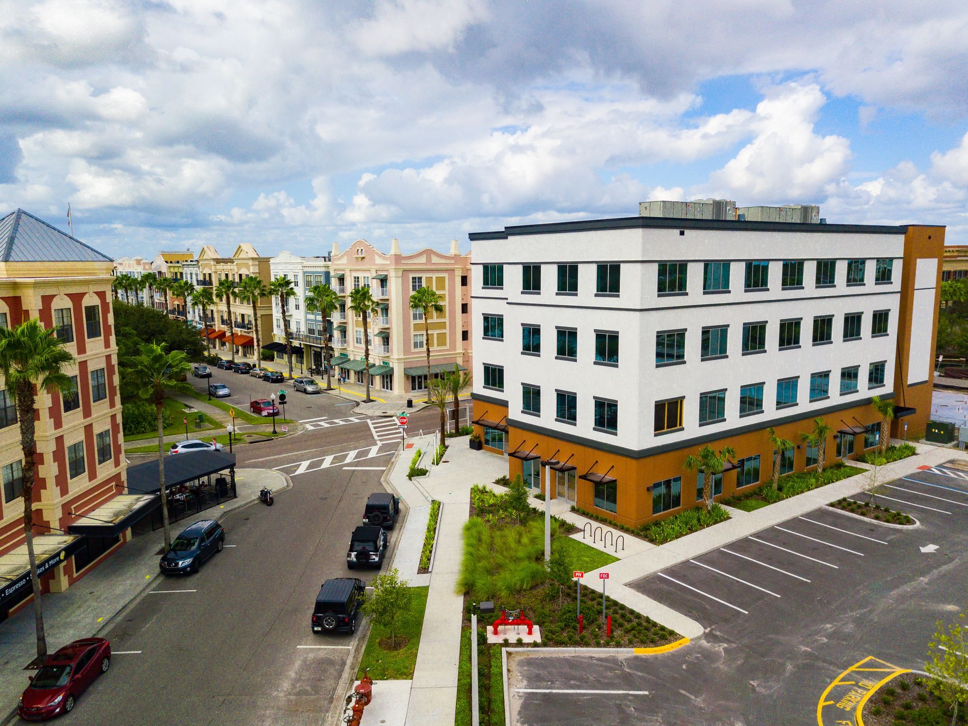 Street with shops and outdoor seating; palm trees and cars are visible.