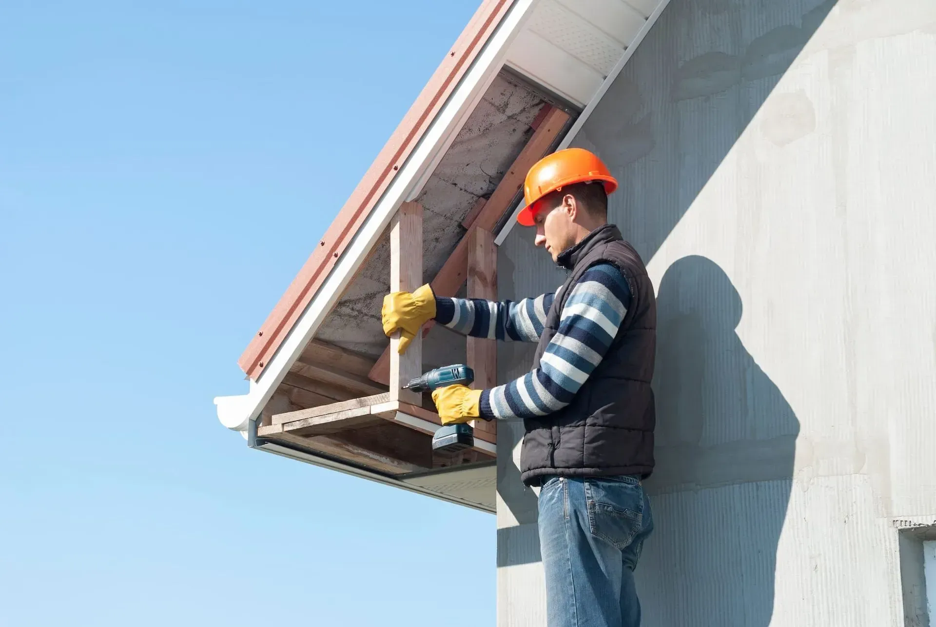 Roofer hammering on a roof. Wearing safety gear, working outdoors with mountains in the background.