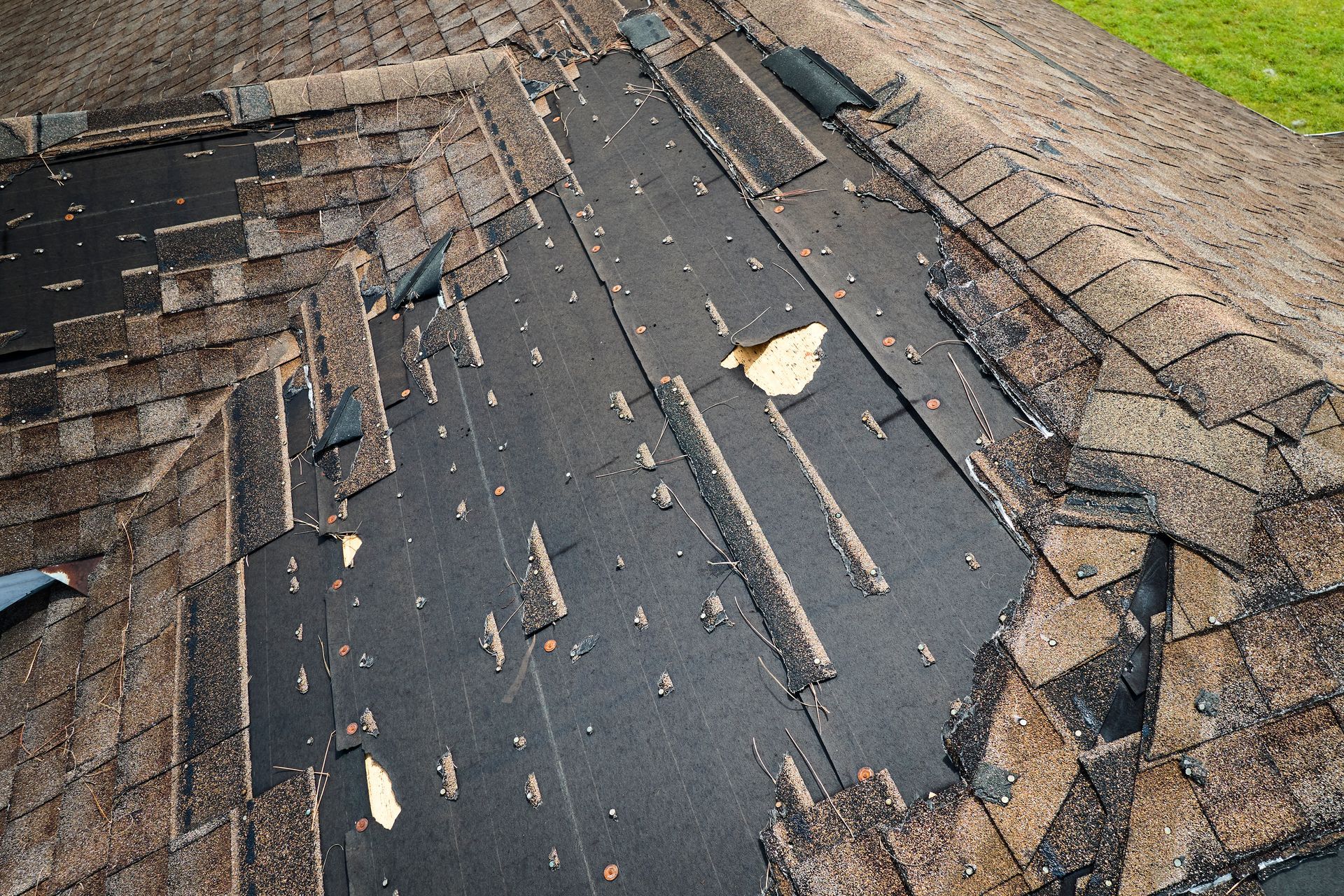 Damaged asphalt shingle roof, with missing shingles and exposed underlayment.