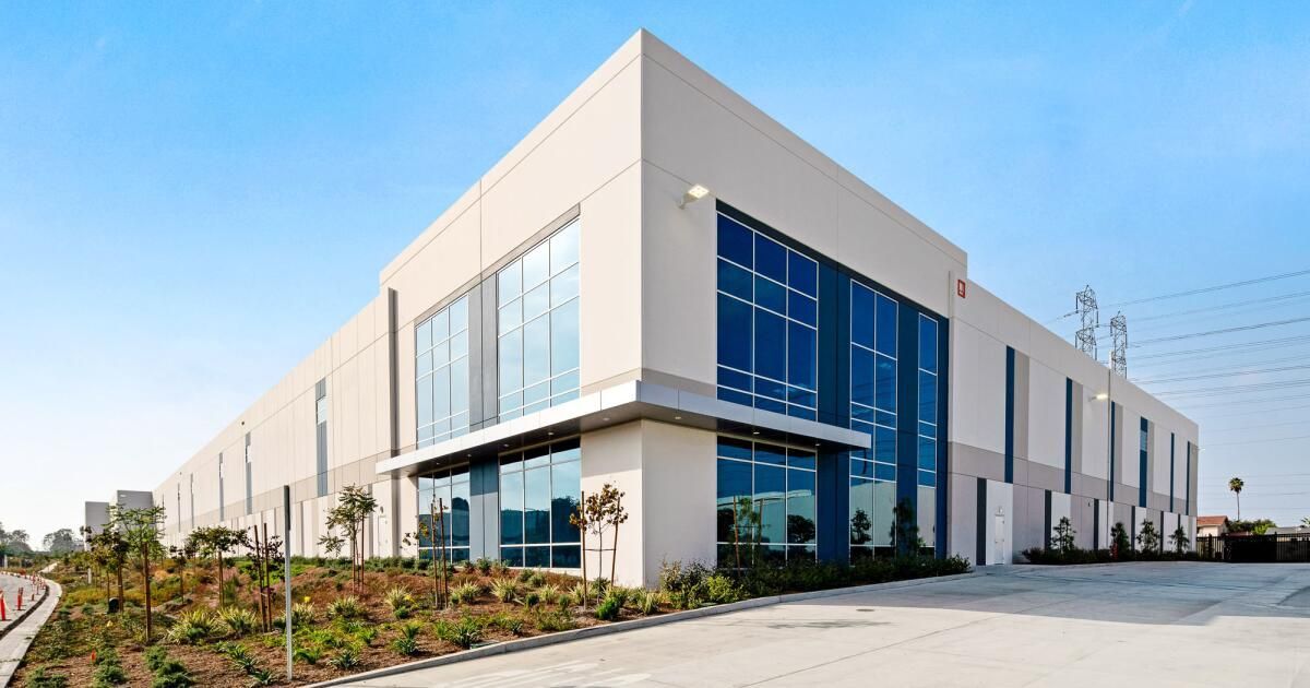 Modern office building with blue-tinted windows, a grassy lawn, and mountains in the background. 