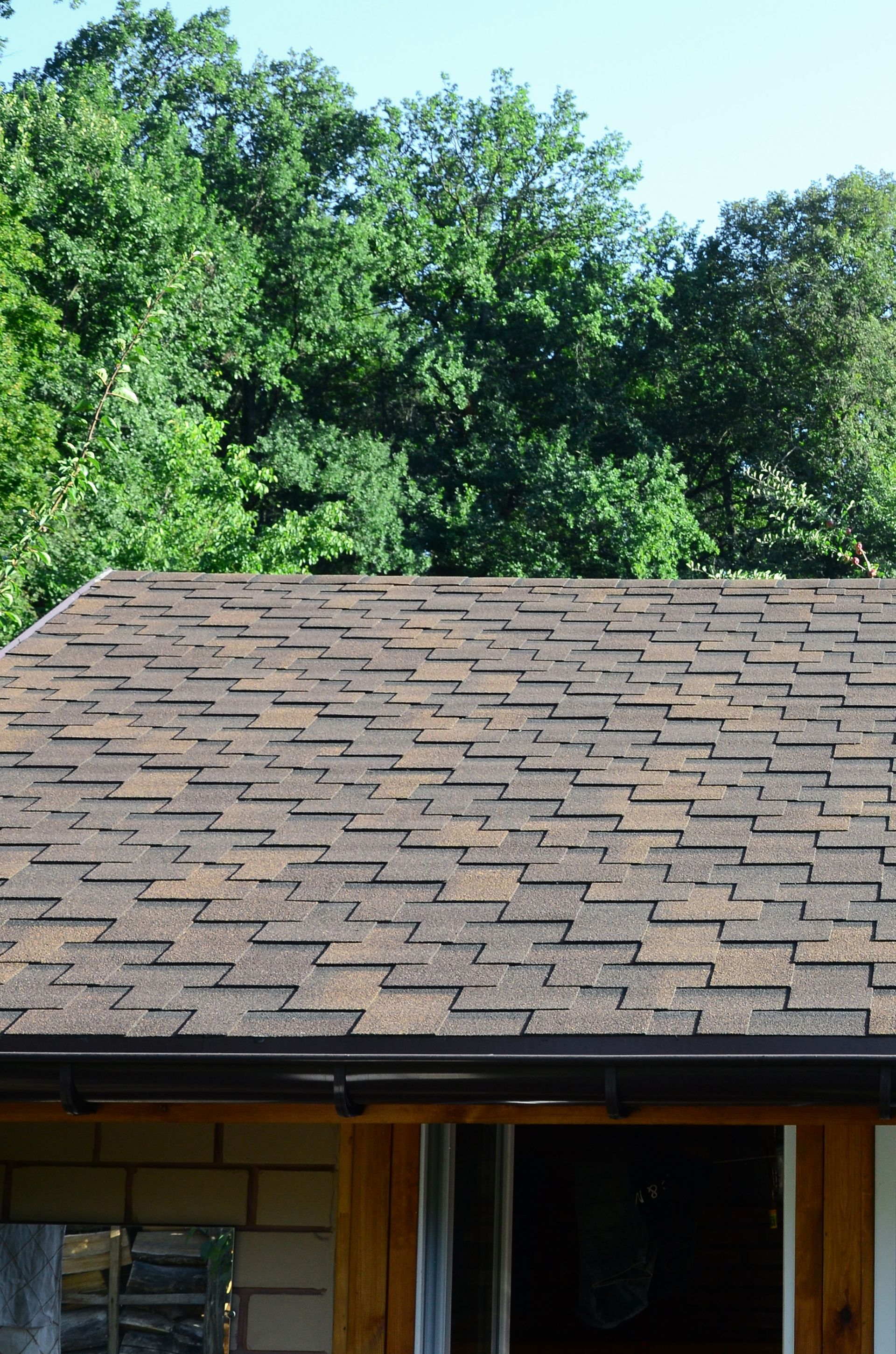Brown shingled roof with a dark eave, and green trees in the background under a blue sky.