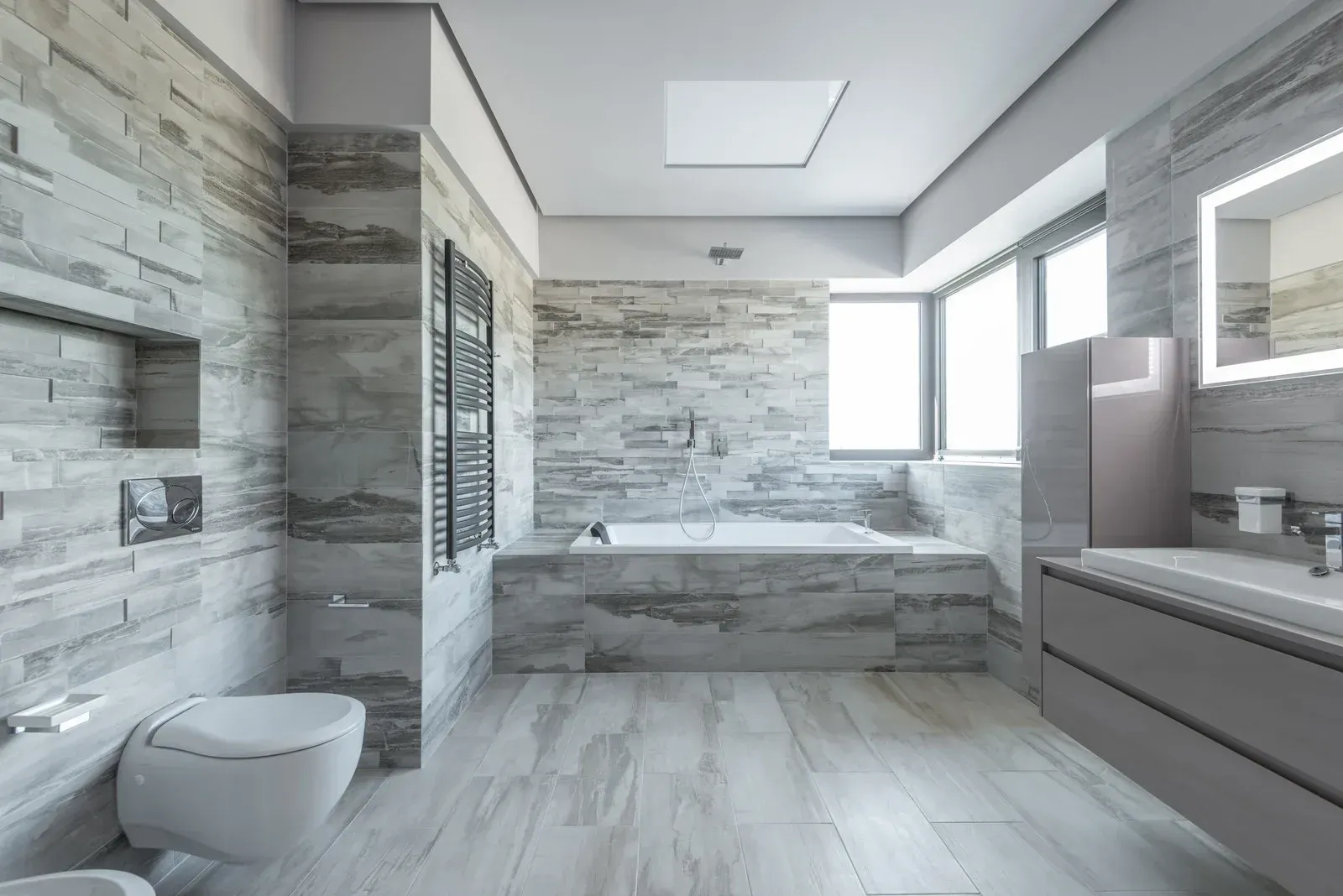 Modern, neutral-toned bathroom with stone-textured walls, a soaking tub, and a floating vanity.