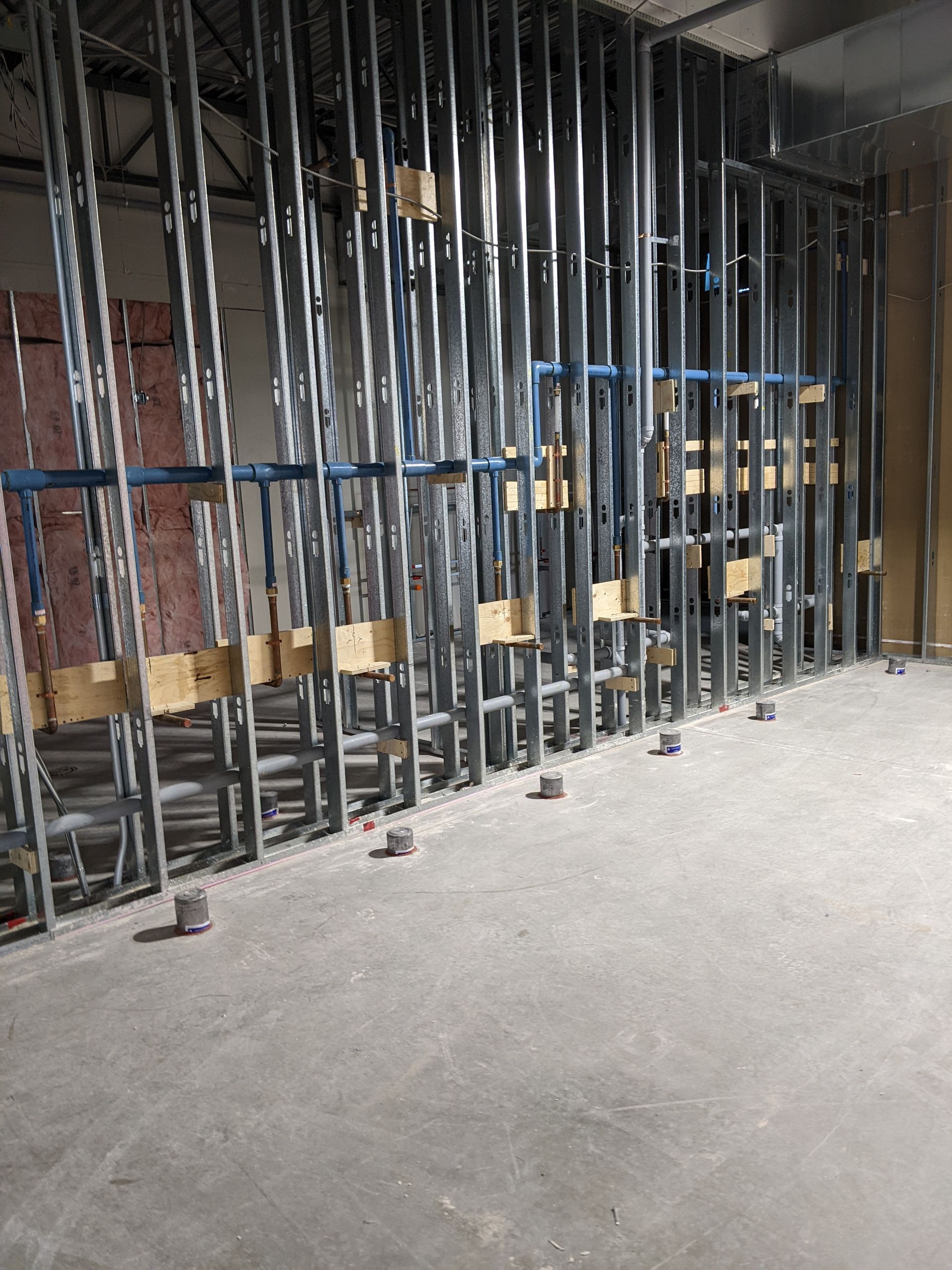 Ossature métallique apparente et entretoises bleues dans un intérieur en construction inachevée