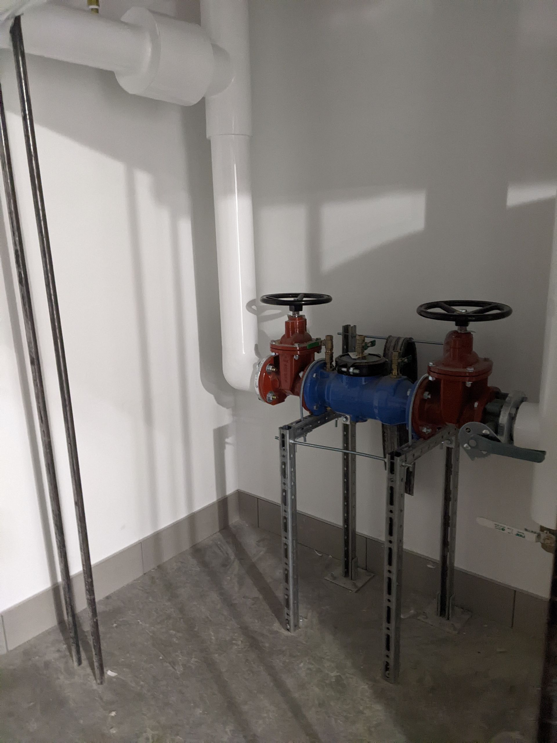 Robinets industriels dans un local technique avec tuyauterie blanche et une section de tuyau bleue.