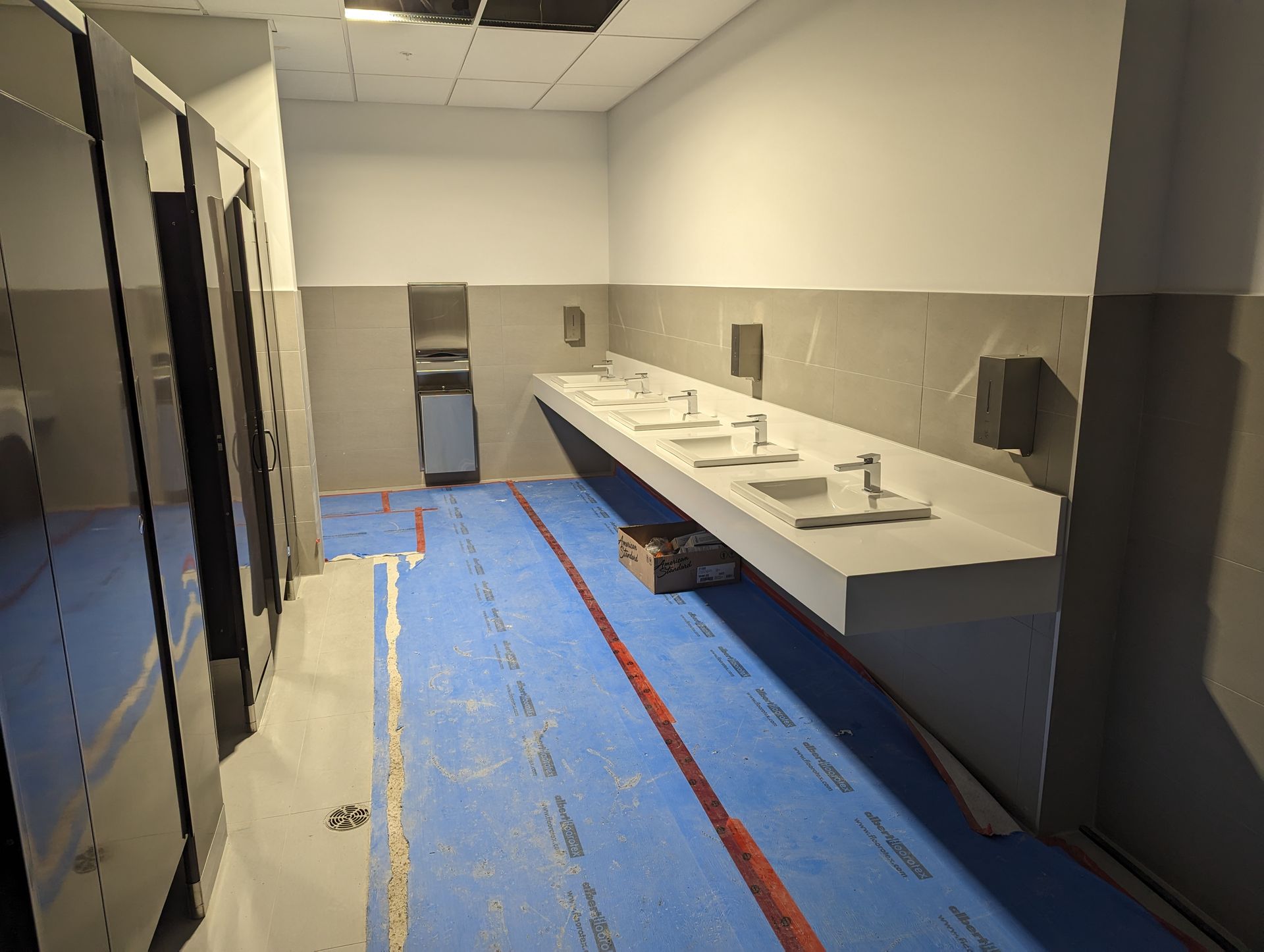 Salle de bain endommagée avec revêtement de sol bleu, lavabos et miroirs, probablement en cours de rénovation