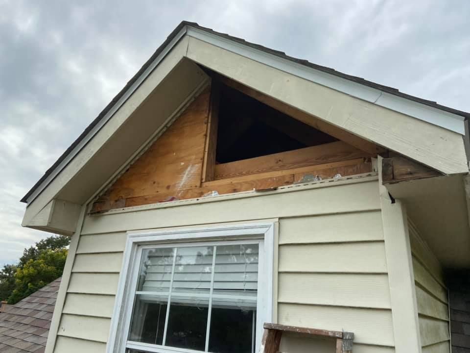 Exterior view of a house with a partially open gable, exposing wooden framing and siding.