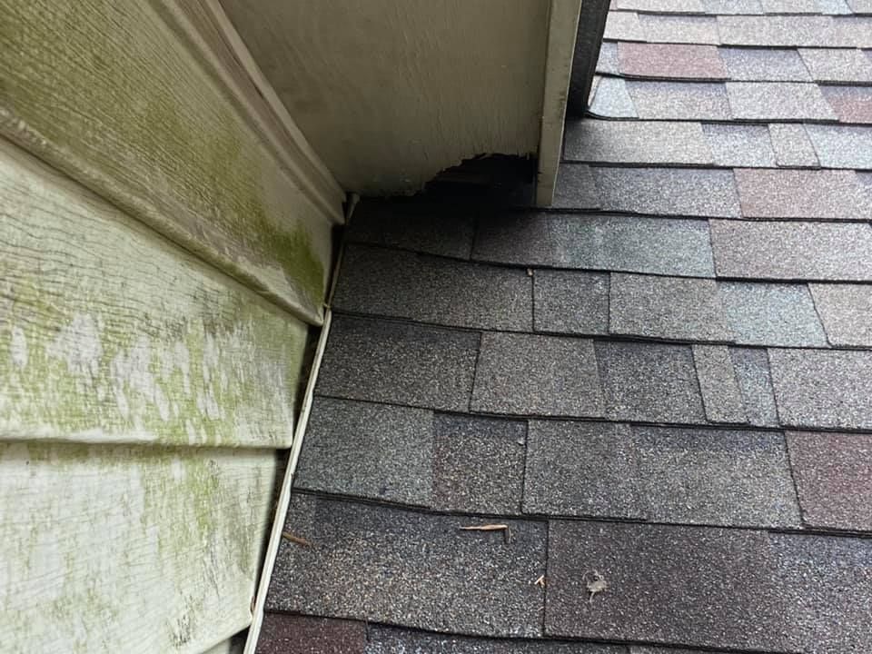 Close-up of a roof with asphalt shingles meeting a siding wall, showing wear and possible water damage.