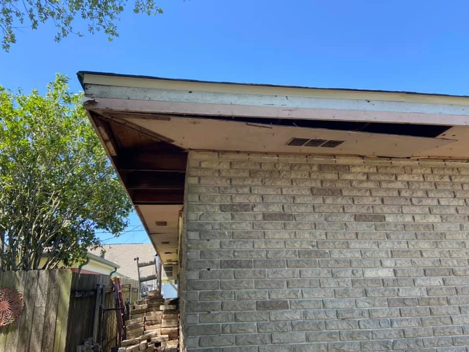 Damaged roof overhang on a brick building with exposed wood and a clear blue sky.