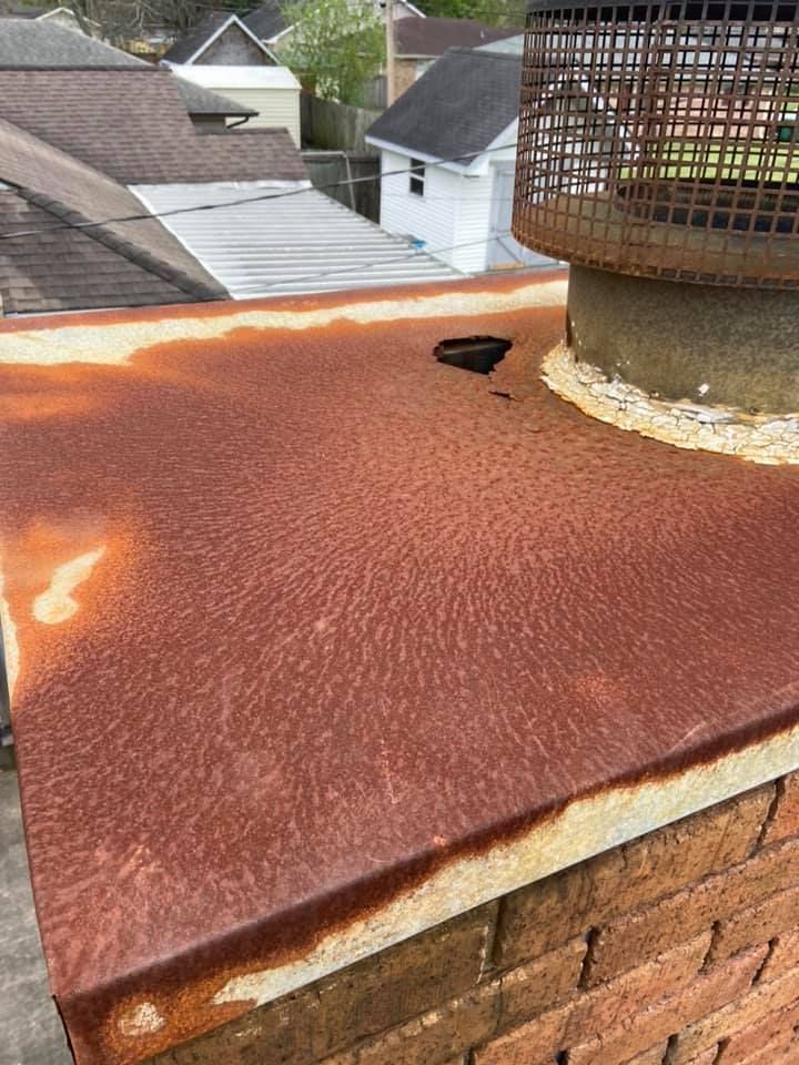 Rusty, weathered metal top of a brick chimney.  A wire mesh chimney cap sits above.