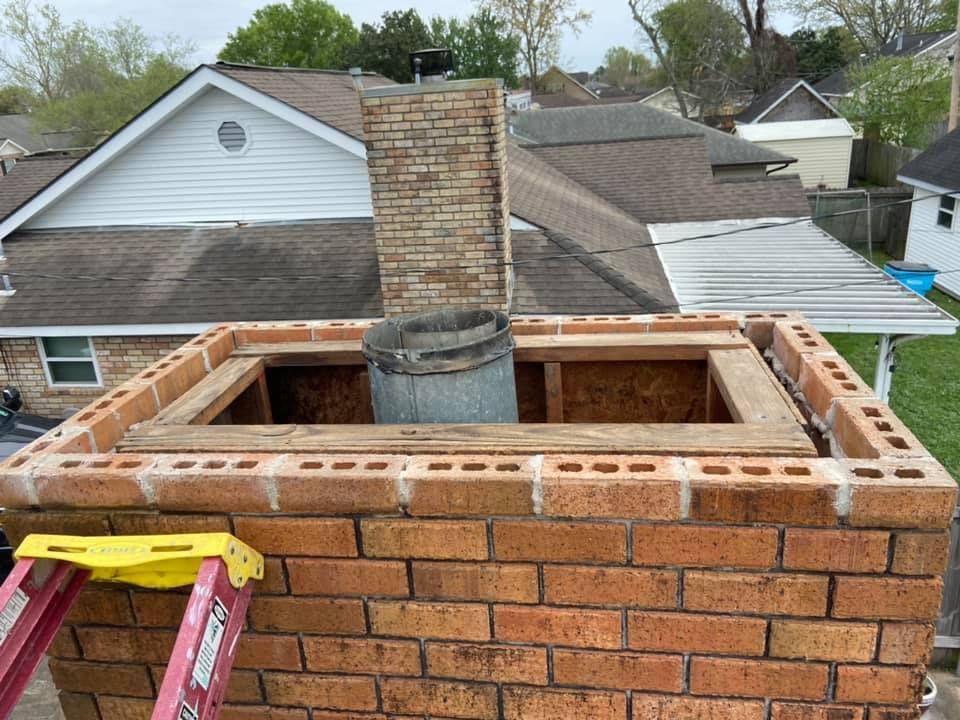 Brick chimney under construction on a rooftop; a ladder is present.