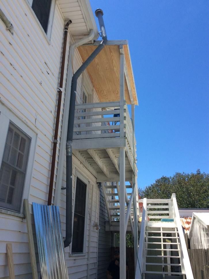White wooden exterior stairs and balcony attached to a two-story house, with a dark gutter.