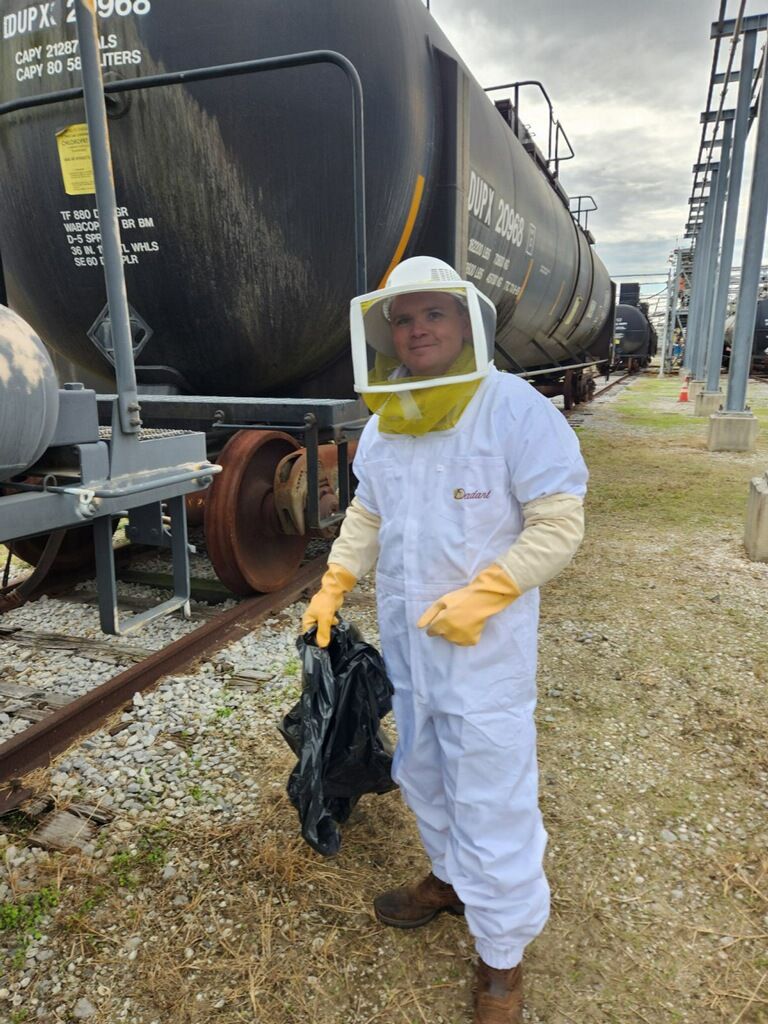 Person in a protective suit holding a trash bag near a train car.