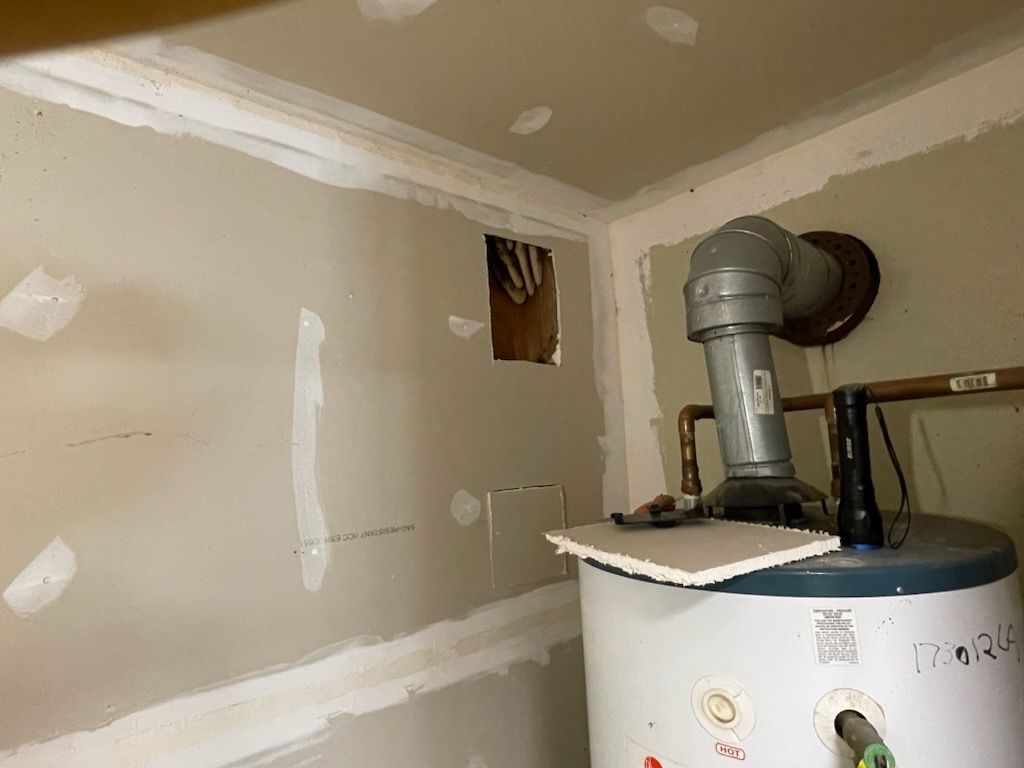 Water heater in a room with patched drywall; ductwork, visible plumbing.