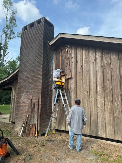 Men removing wooden siding from a building, with a brick chimney on the left.