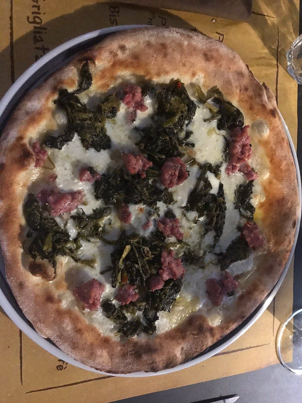 Una pizza dalla crosta sottile condita con formaggio bianco fuso, verdure a foglia verde scuro e pezzi di salsiccia saporita.
