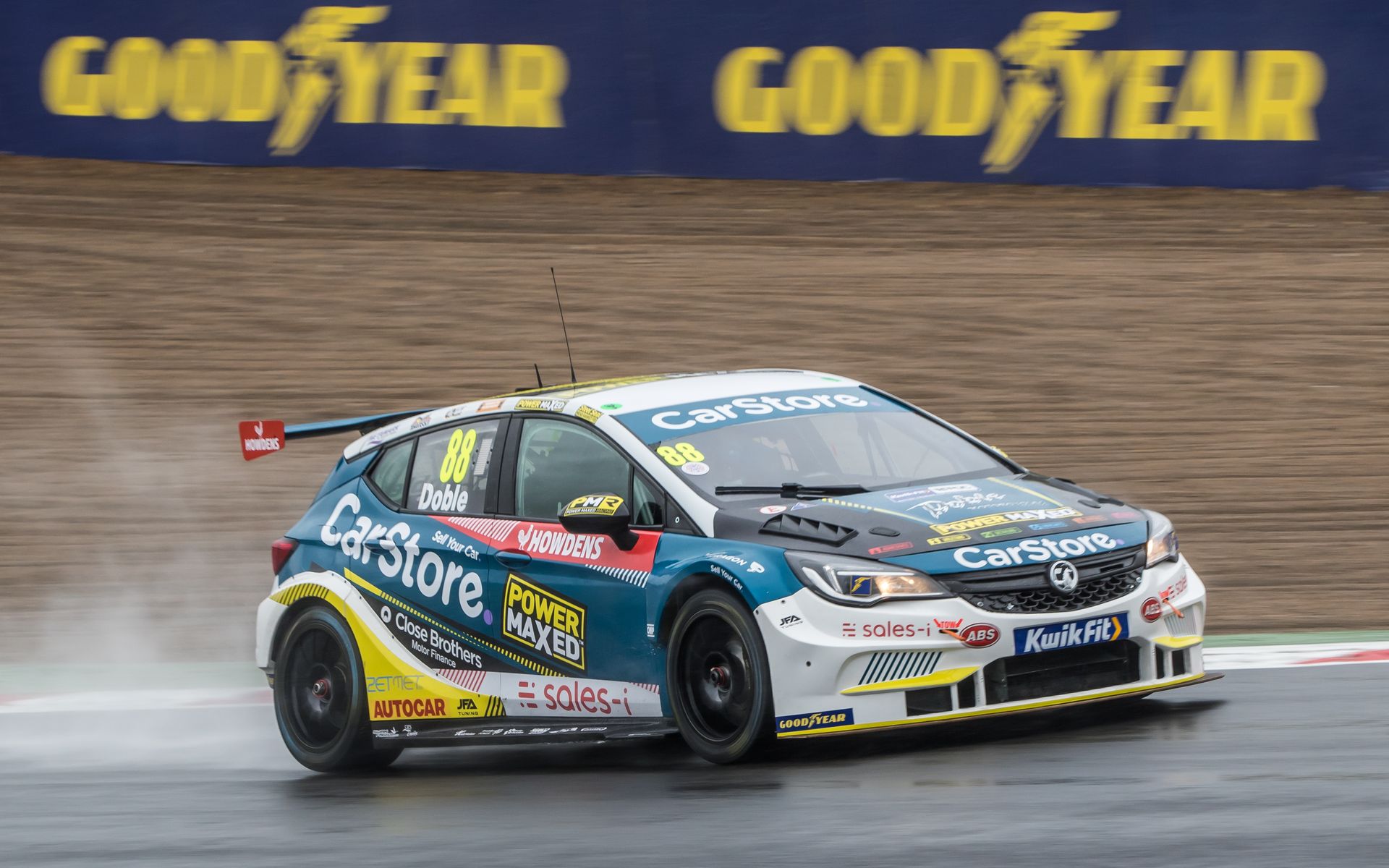 A race car is driving down a wet track in front of a good year sign.