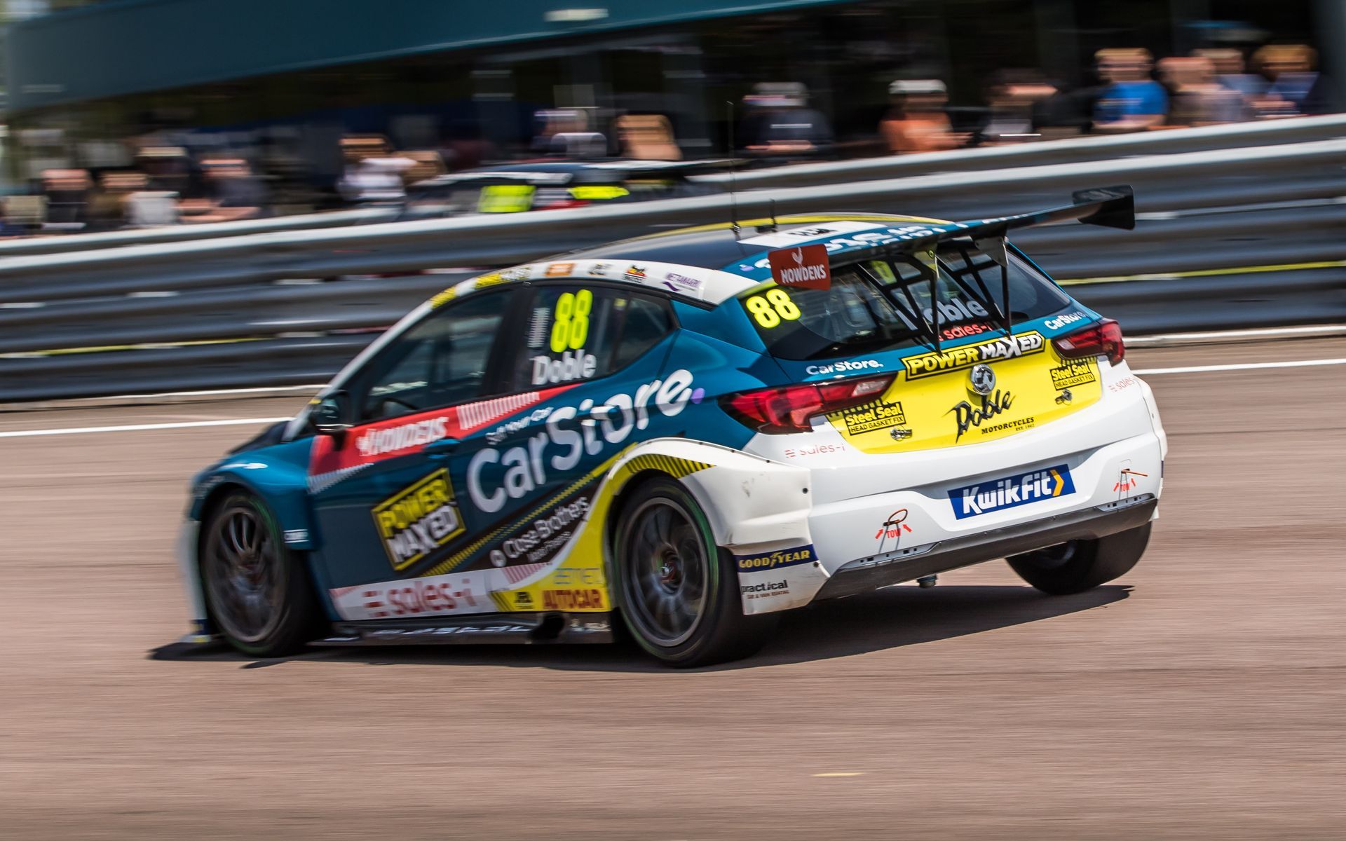 A blue and yellow race car is driving down a race track.