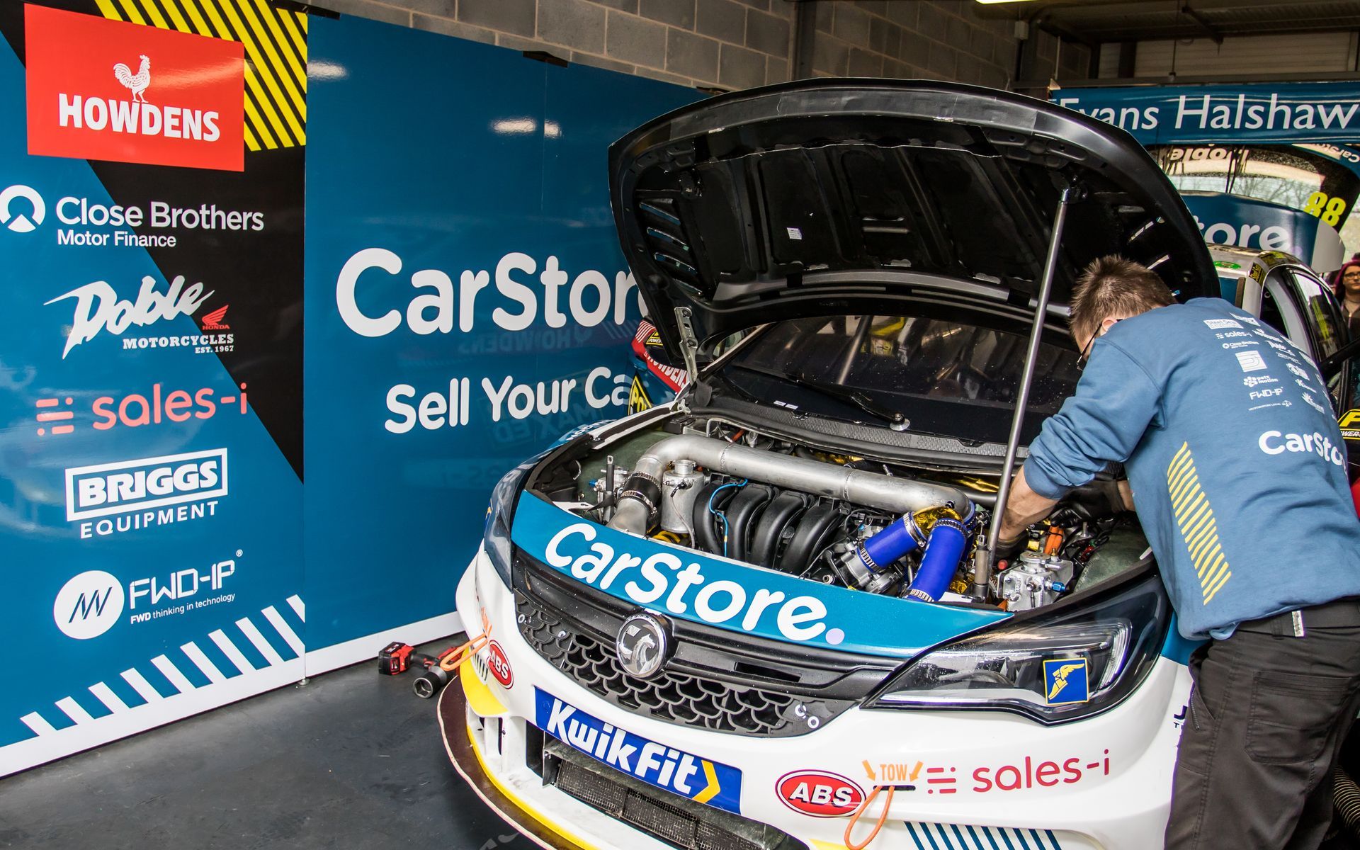 A man is working on a race car with the hood open