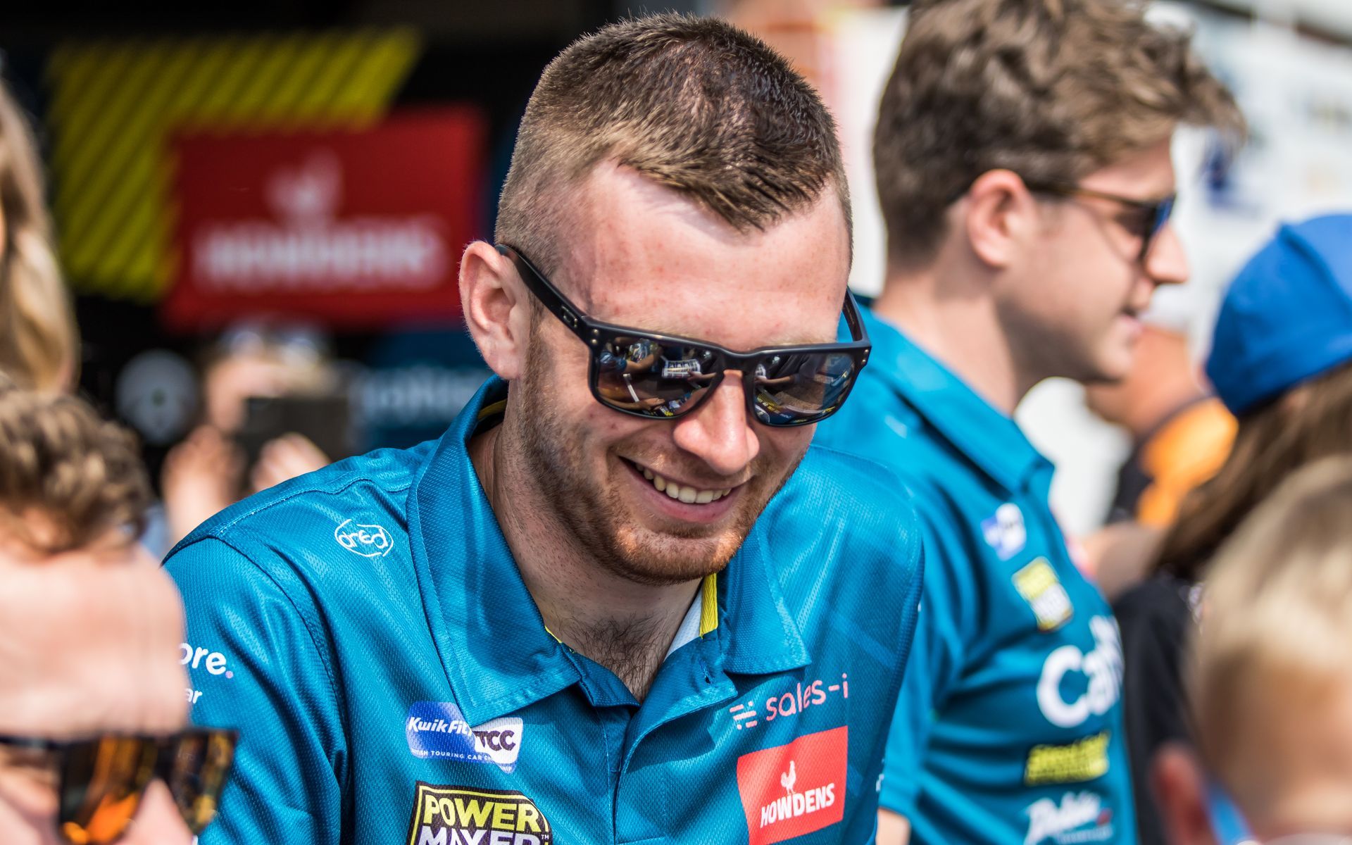 A man wearing sunglasses and a blue shirt is smiling.