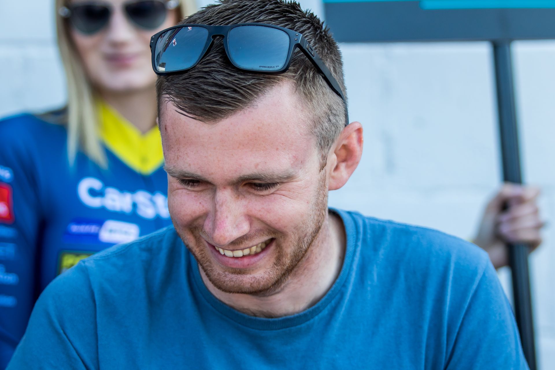 A man wearing sunglasses and a blue shirt is smiling.