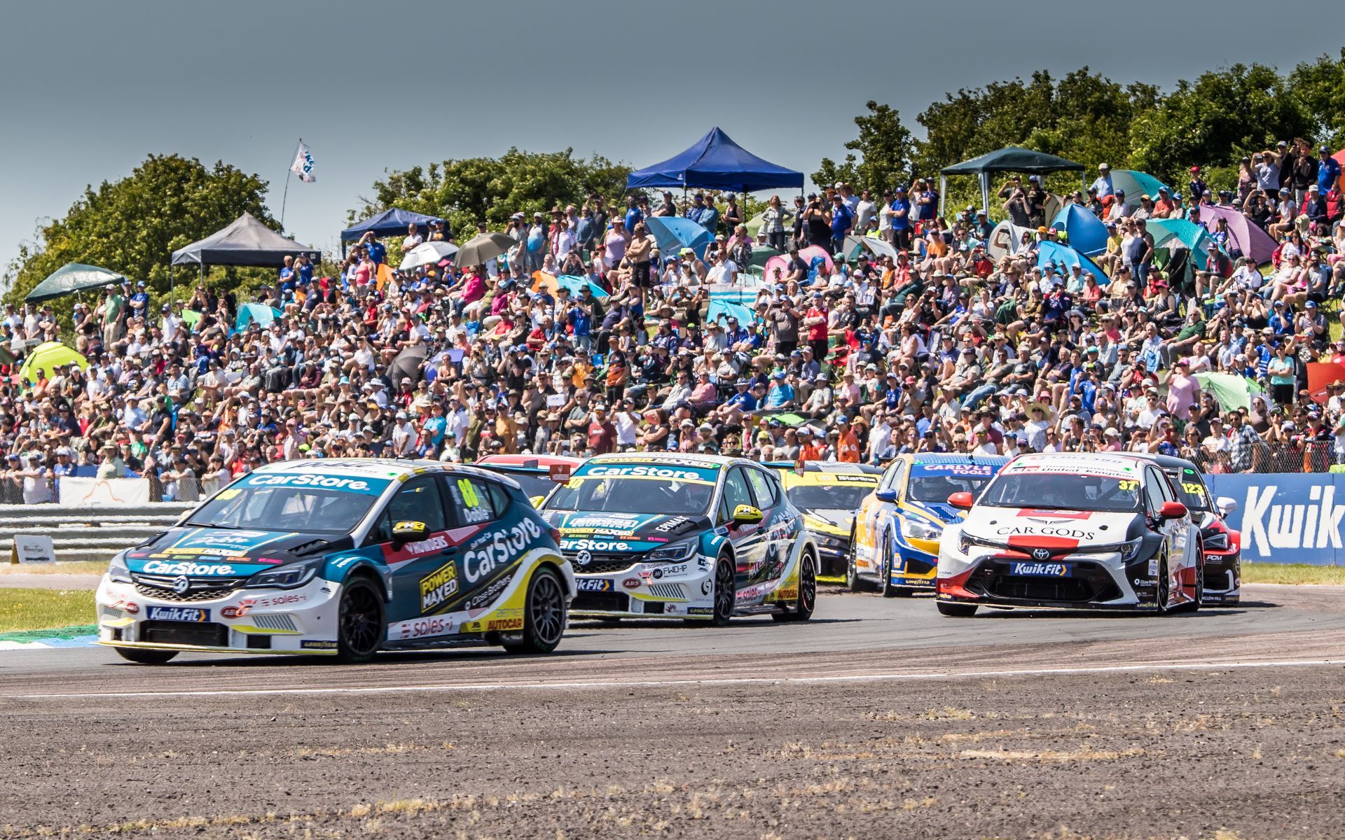A group of cars are racing on a race track in front of a crowd.