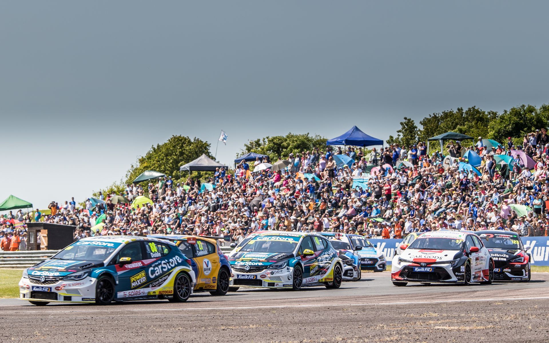 A group of cars are racing on a race track in front of a crowd.