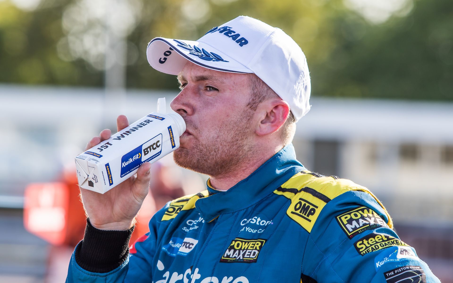 A man in a racing suit is drinking from a cup.