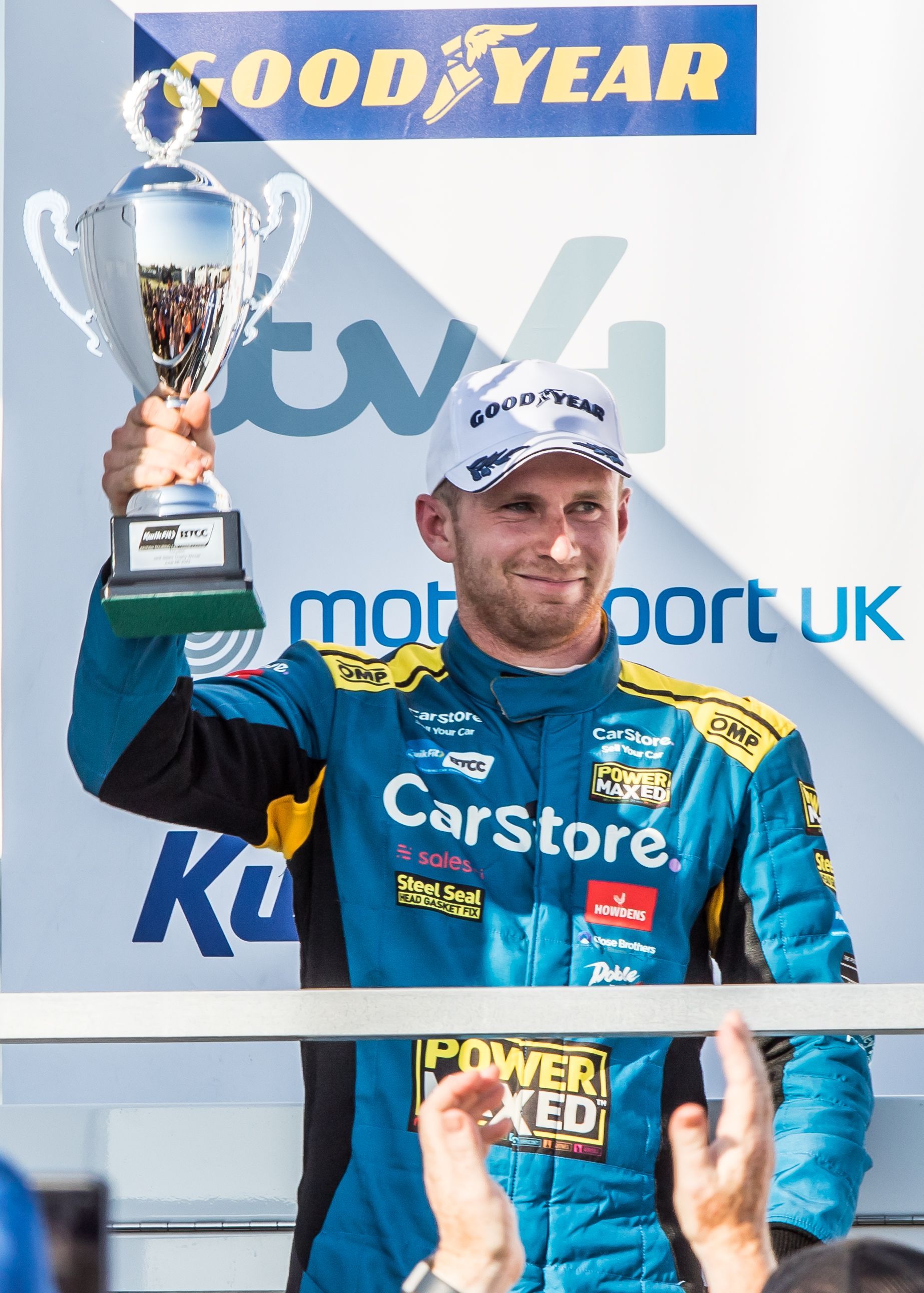A man in a car store uniform is holding a trophy