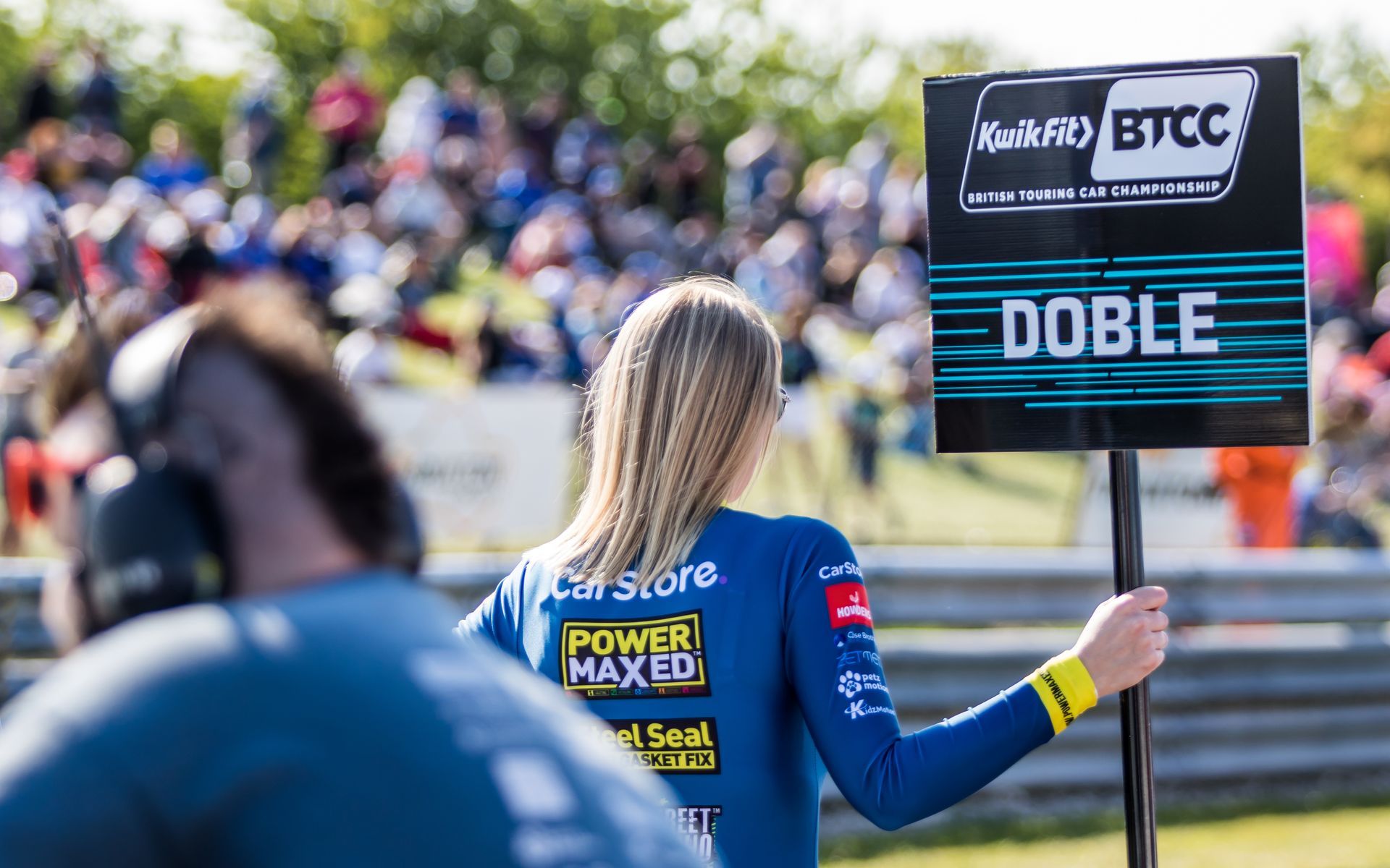 A woman is holding a sign that says doble in front of a crowd.