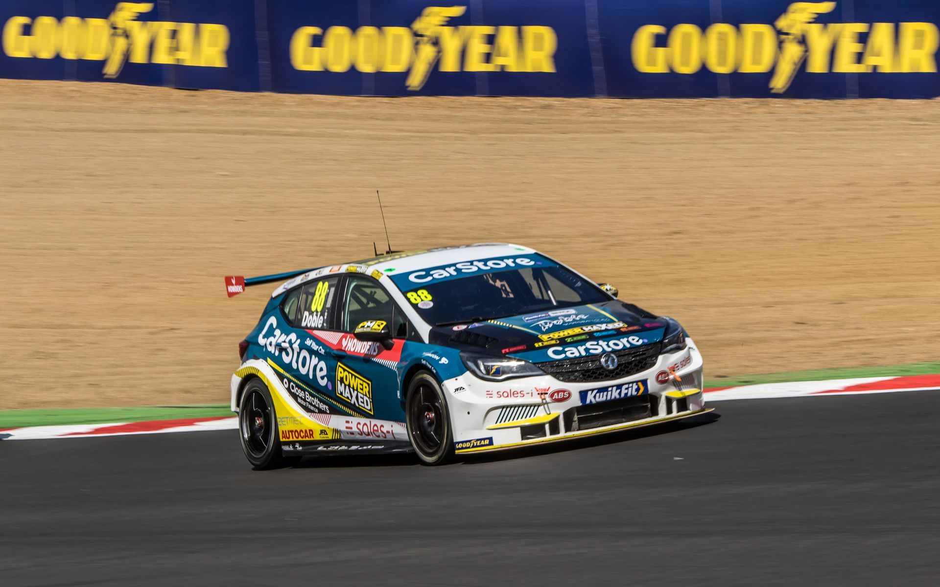 A race car is driving on a track with a good year banner in the background.