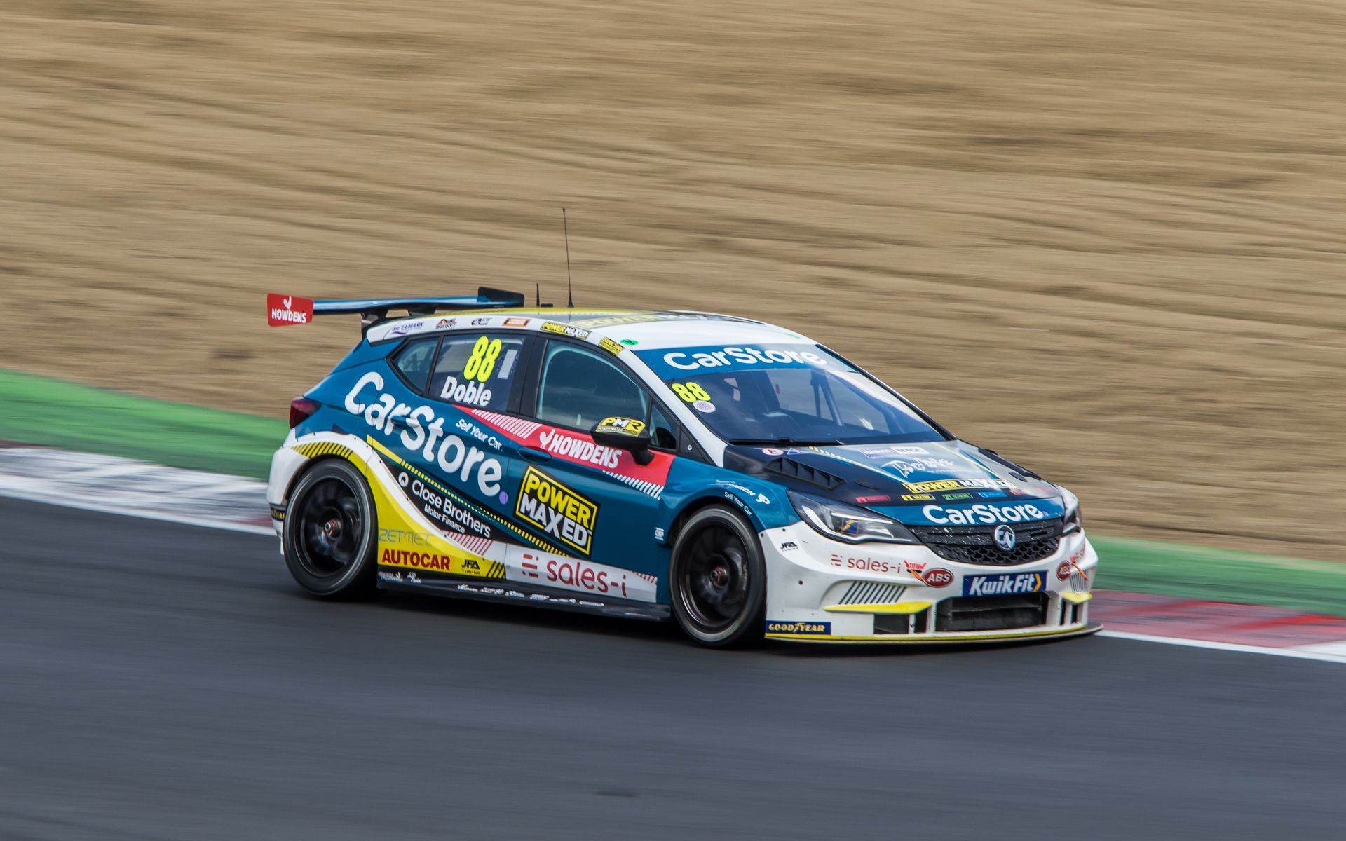 A blue and yellow race car is driving down a race track.