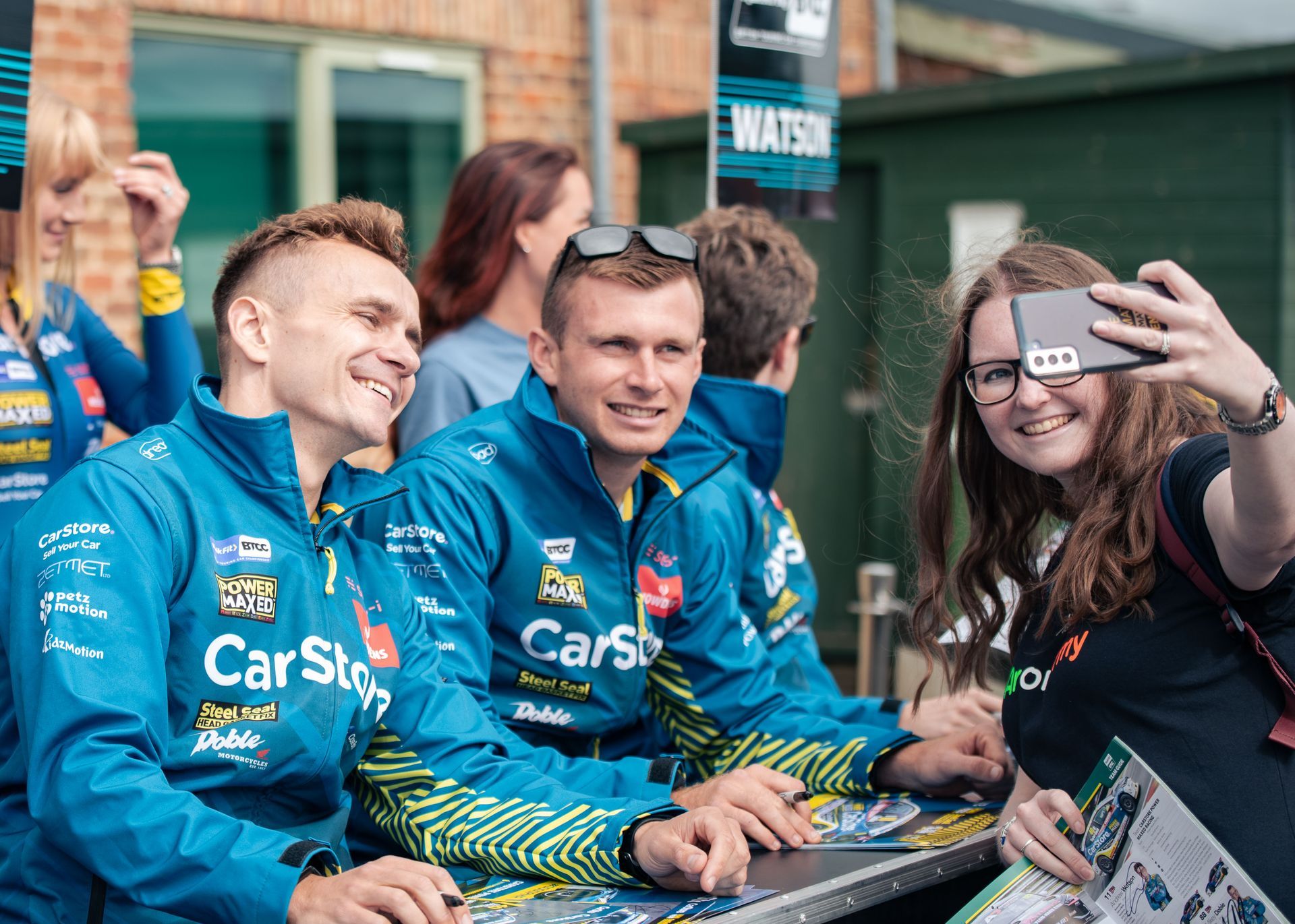A woman is taking a selfie with a group of people wearing blue jackets.
