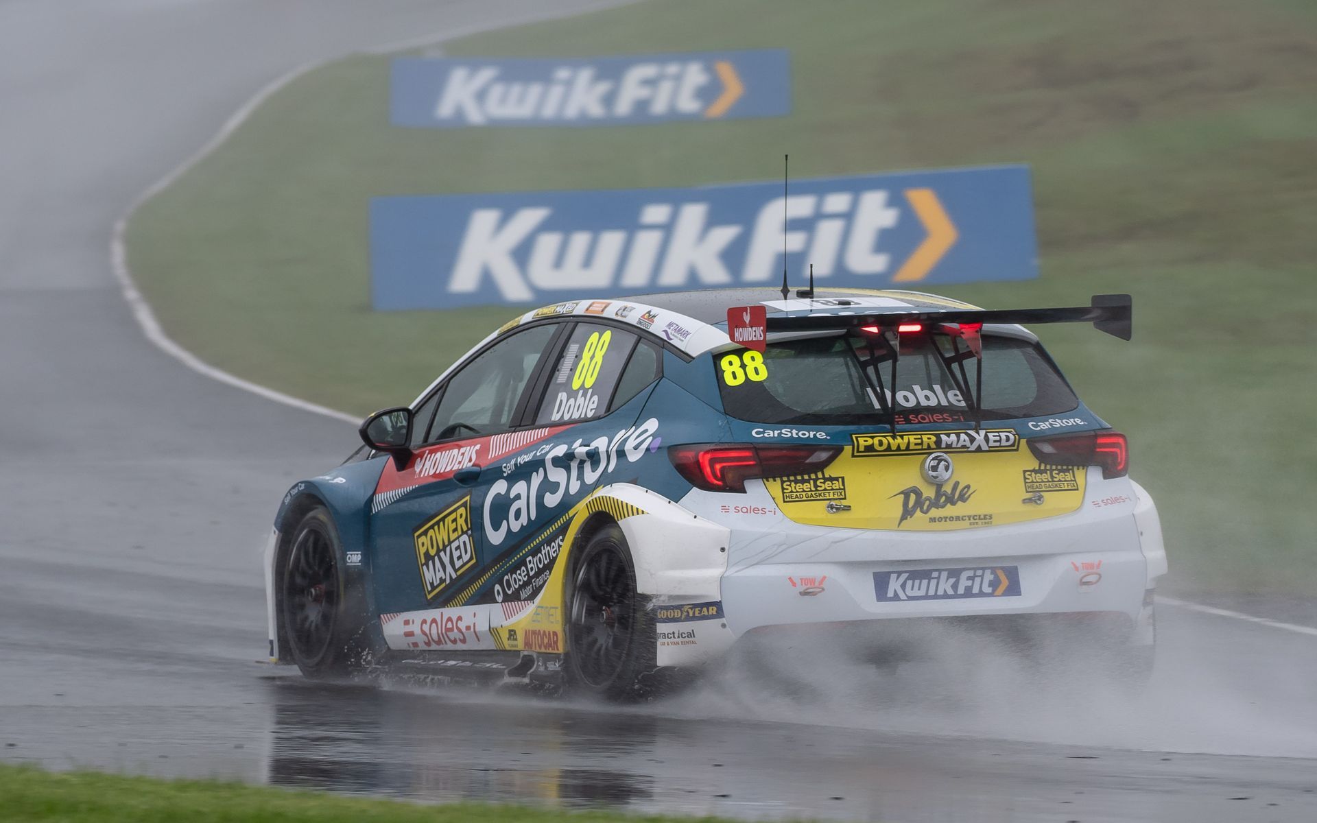 A race car is driving on a wet track in the rain.