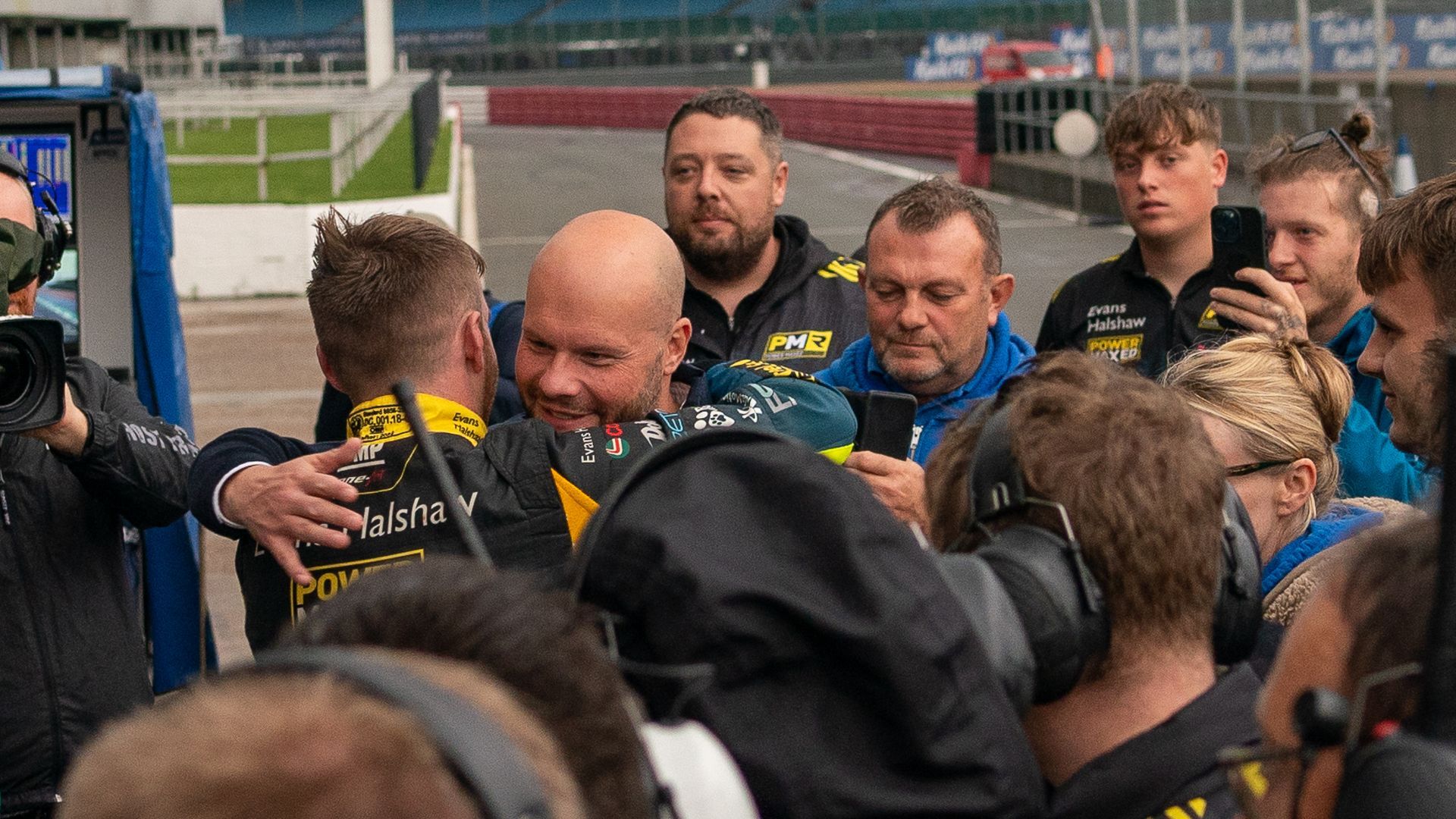 A group of men are hugging each other on a race track.